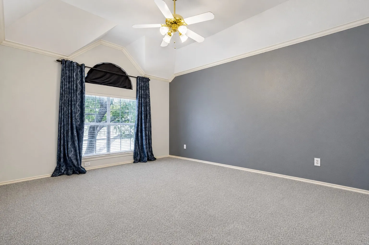 Vaulted ceiling room featuring a large window with an arched transom, light gray carpeting, and a ceiling fan