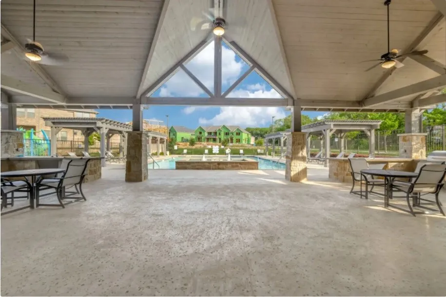 Community Spacious covered outdoor pavilion featuring an exposed beam ceiling, ceiling fans, stone-clad support pillars, and a concrete patio
