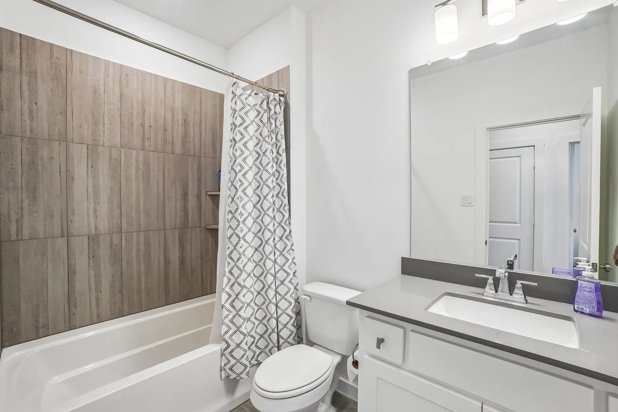 Full bathroom featuring a tub-shower combination with wood-look tile surround, built-in shower niches, a white vanity with a light gray countertop, and a single basin sink with a chrome faucet