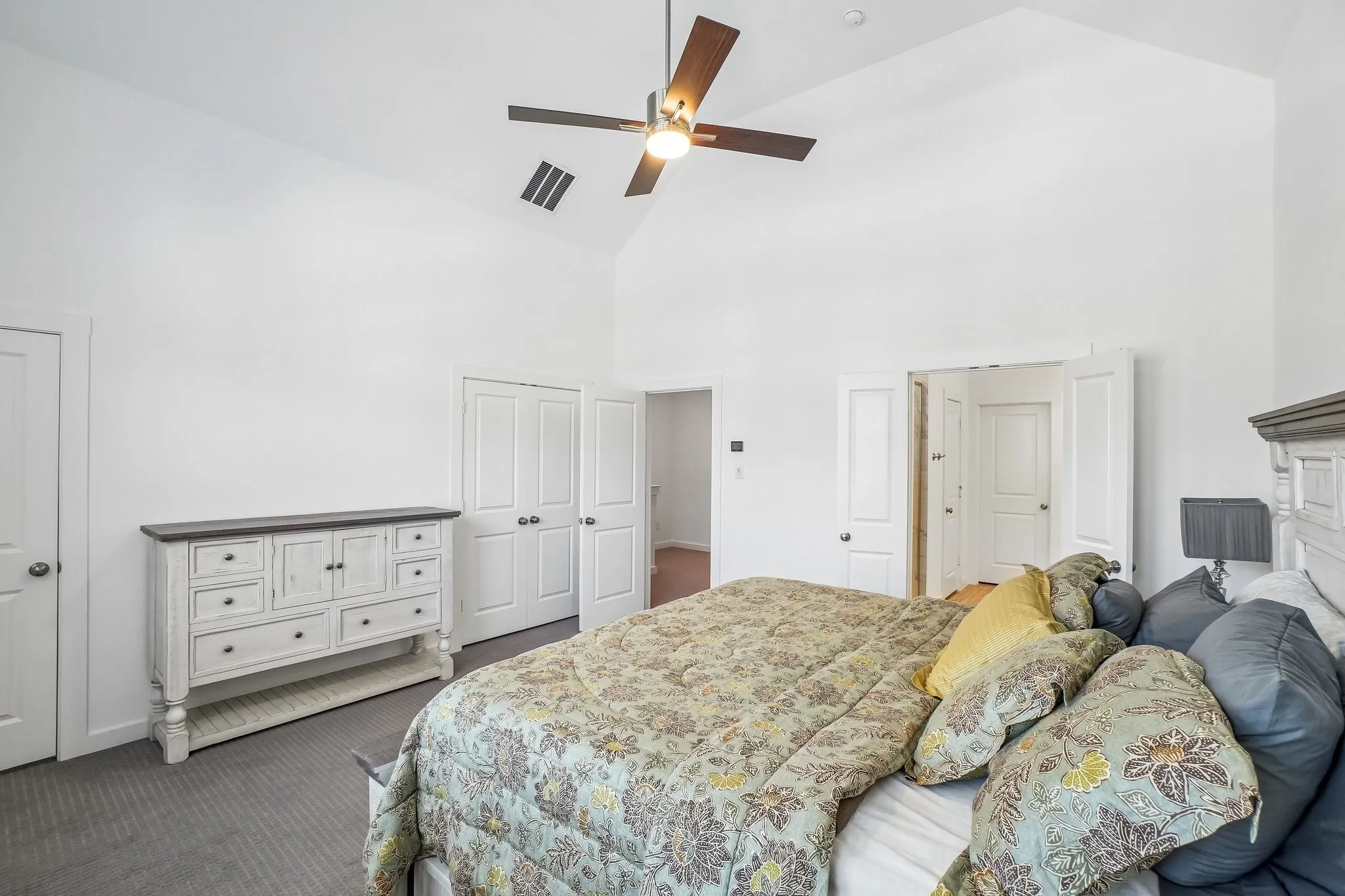 Vaulted ceiling room featuring a ceiling fan with integrated lighting, wood-finish flooring, and multiple white panel doors