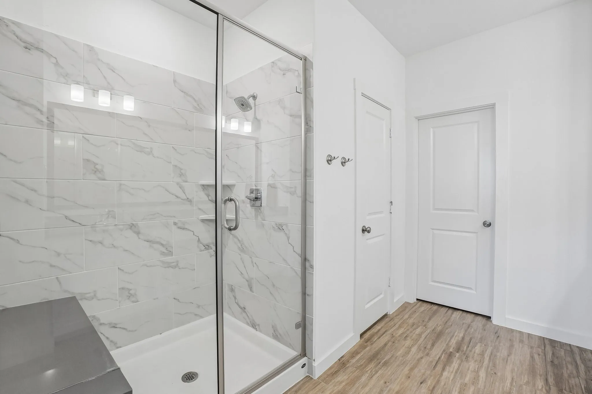 Walk-in shower featuring clear glass enclosure, subway tile with stone-look veining, a built-in shower bench, and a rain showerhead