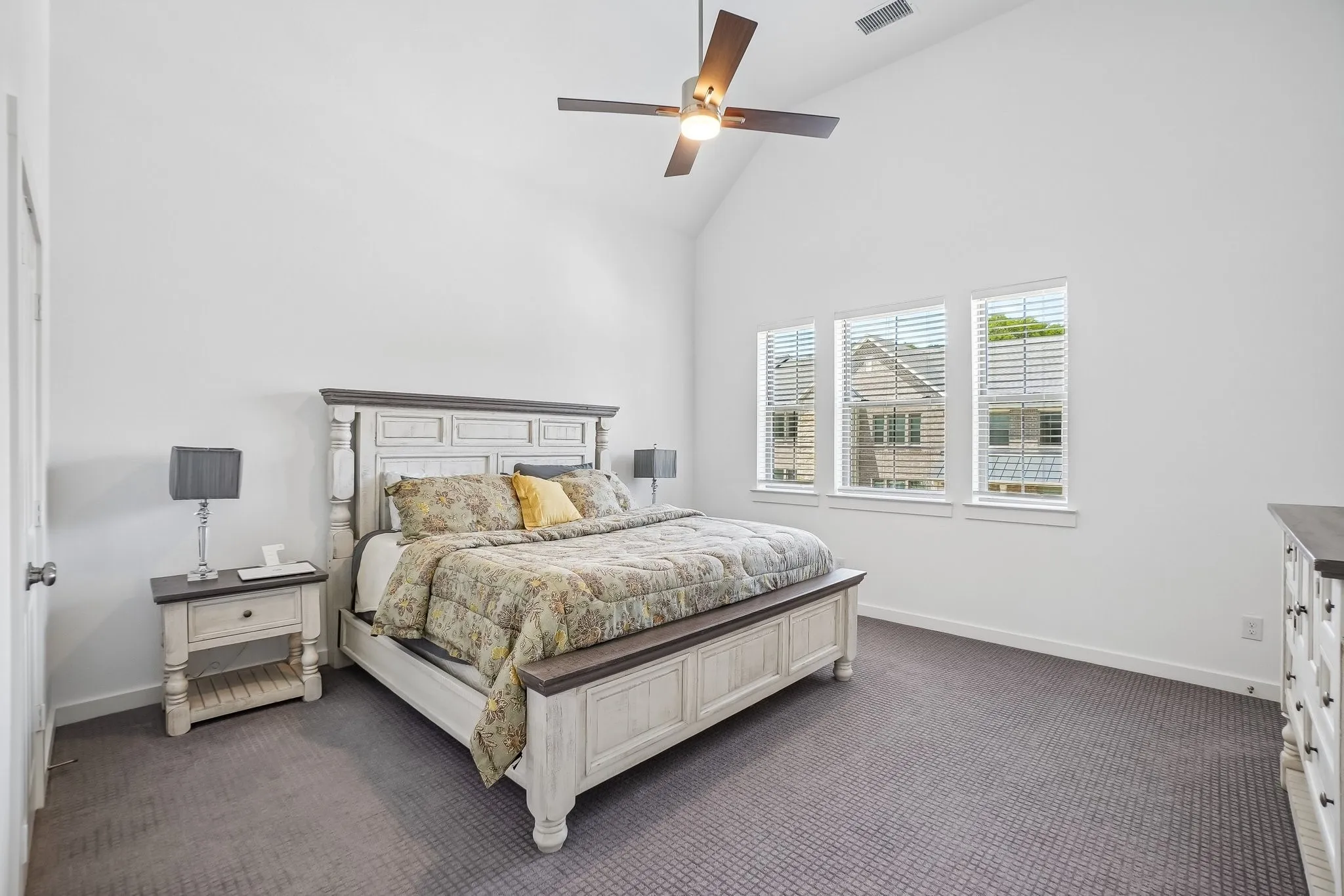 Spacious room featuring a vaulted ceiling with a ceiling fan, three windows with blinds, and gray carpet flooring