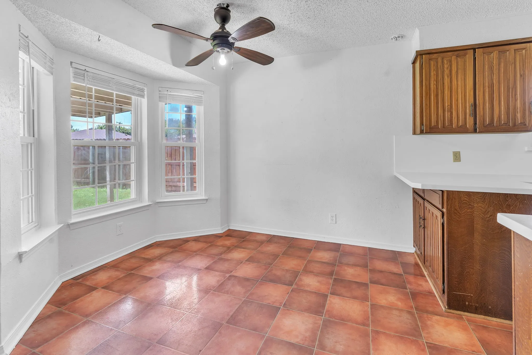 Breakfast nook featuring a bay window, terracotta-style tile flooring, and a ceiling fan