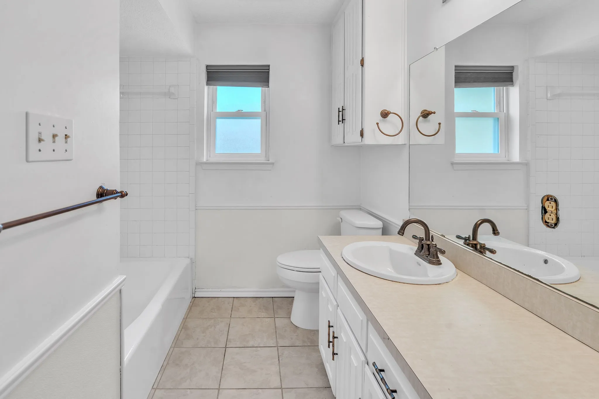 Bathroom featuring a white vanity with integrated sink, a large mirror, and a window with roller shade