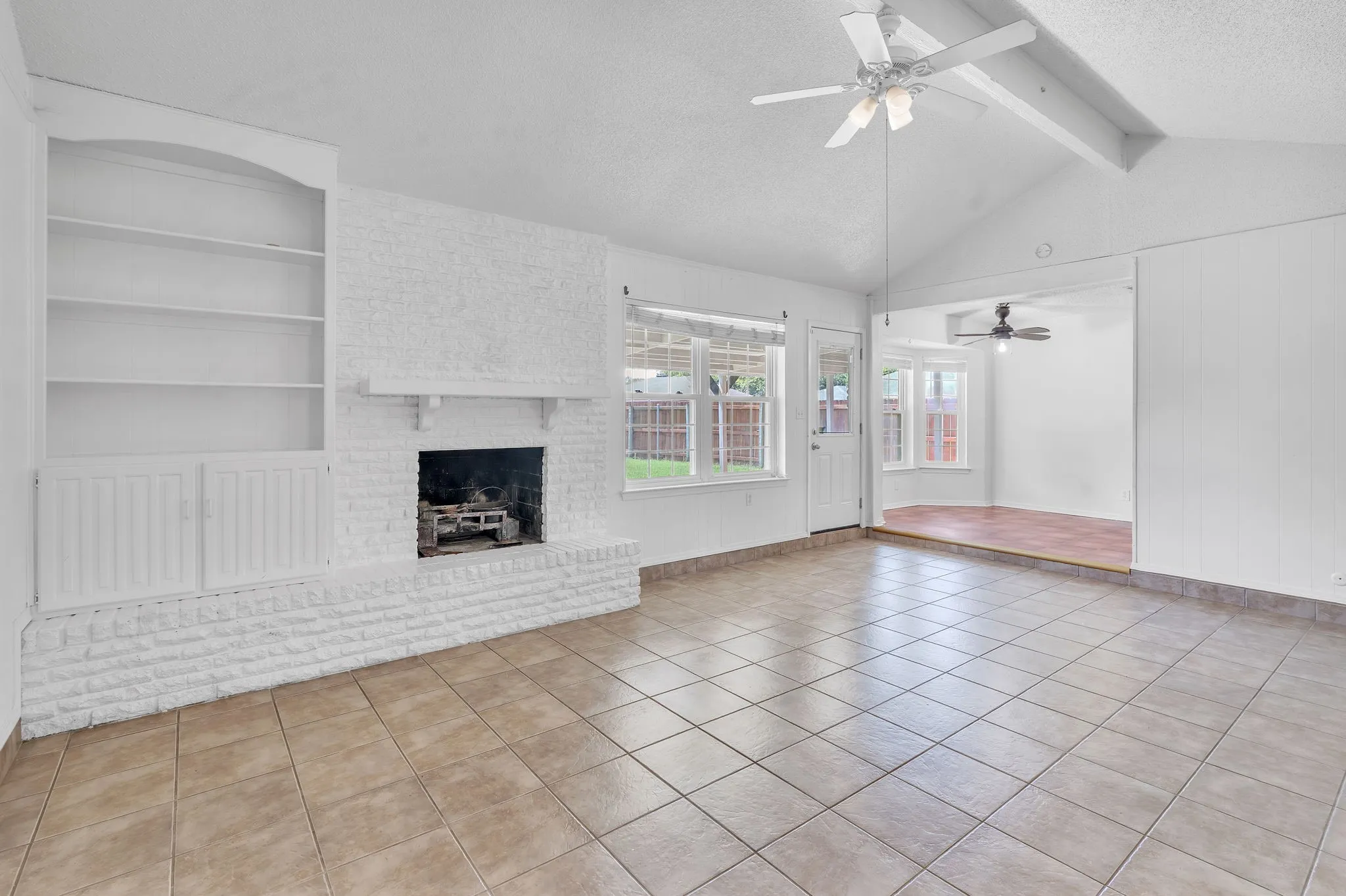 Spacious living area featuring a vaulted ceiling with exposed beams, ceiling fan, and tile flooring