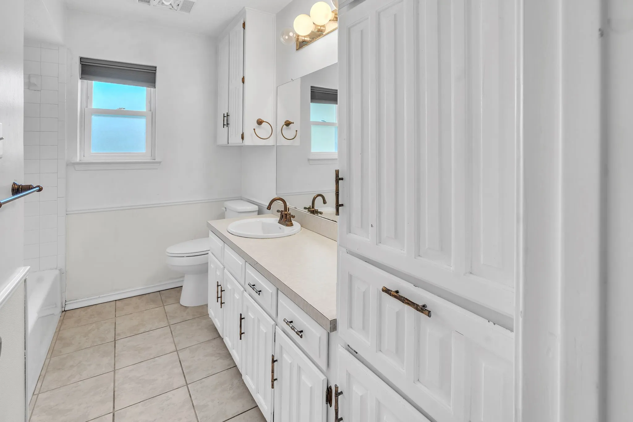 Bathroom featuring a single vanity with white cabinetry, integrated sink, and an extensive built-in linen cabinet