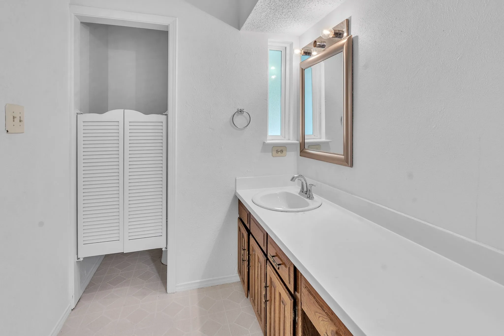 Bathroom featuring an elongated vanity with an integrated sink, wood-finish cabinetry, a framed mirror, and a window