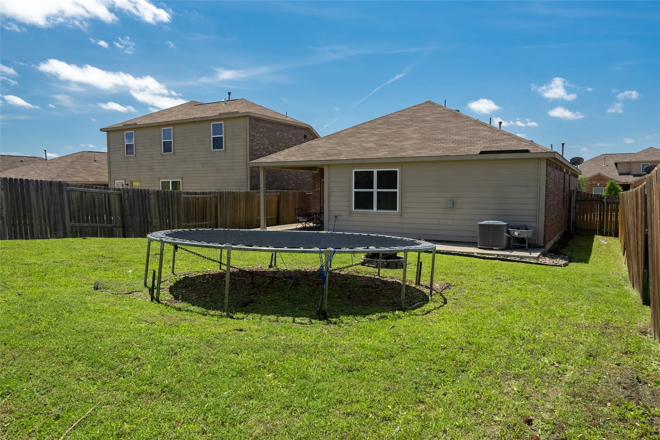 Back of property featuring a yard, a trampoline, and central air condition unit