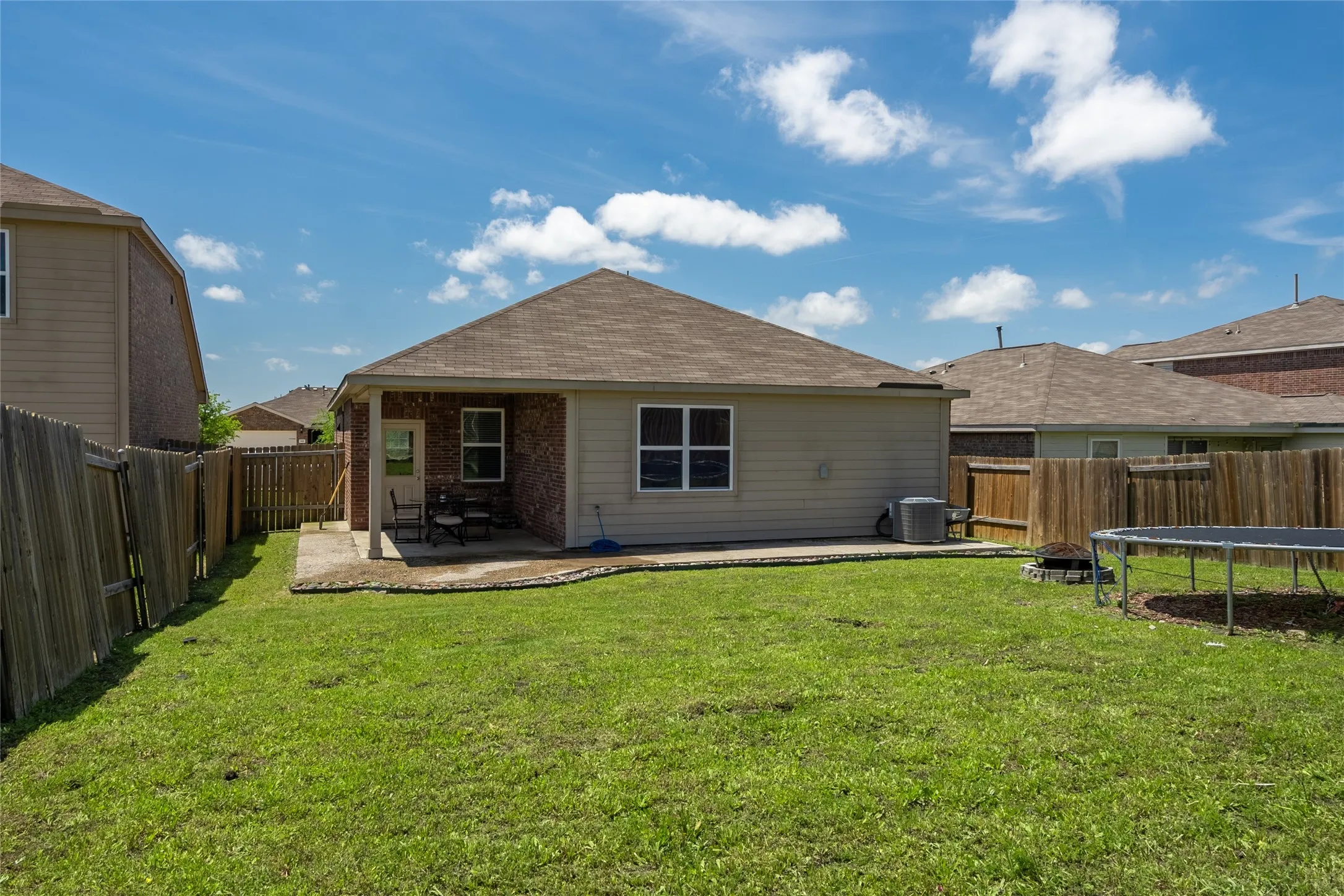 Rear view of property with a trampoline, a yard, and a patio area