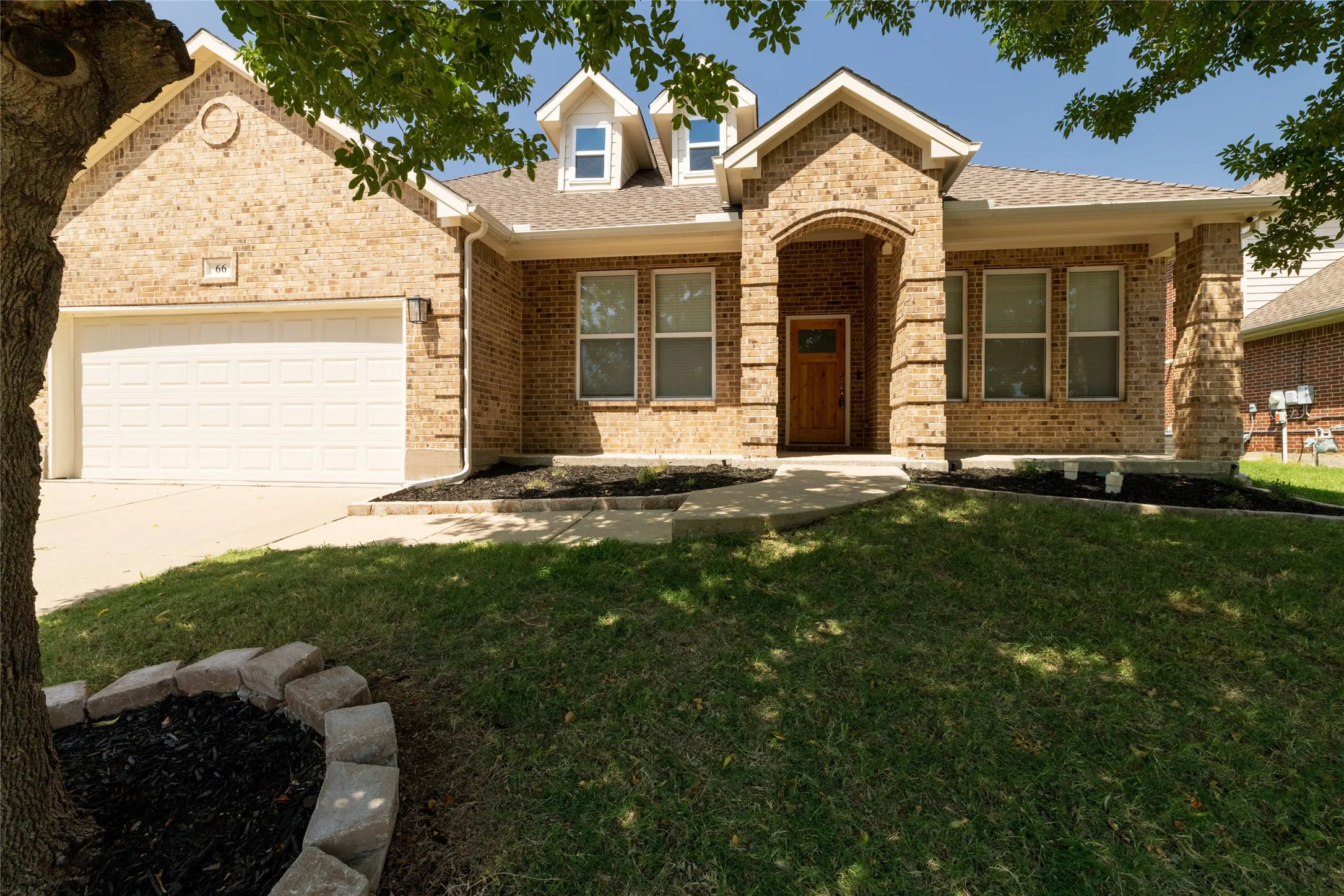ORG Photo used by AI - Brick exterior with an arched entry, dormer windows, and an attached two-car garage