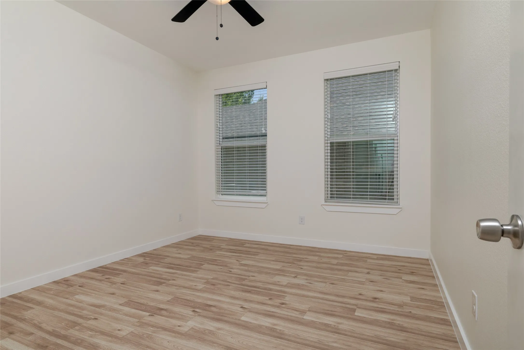 1 of 2 bedrooms at back of house - great for family or guest who want their privacy - Bright room featuring wood-finish flooring, two windows with blinds, a ceiling fan, and white baseboards