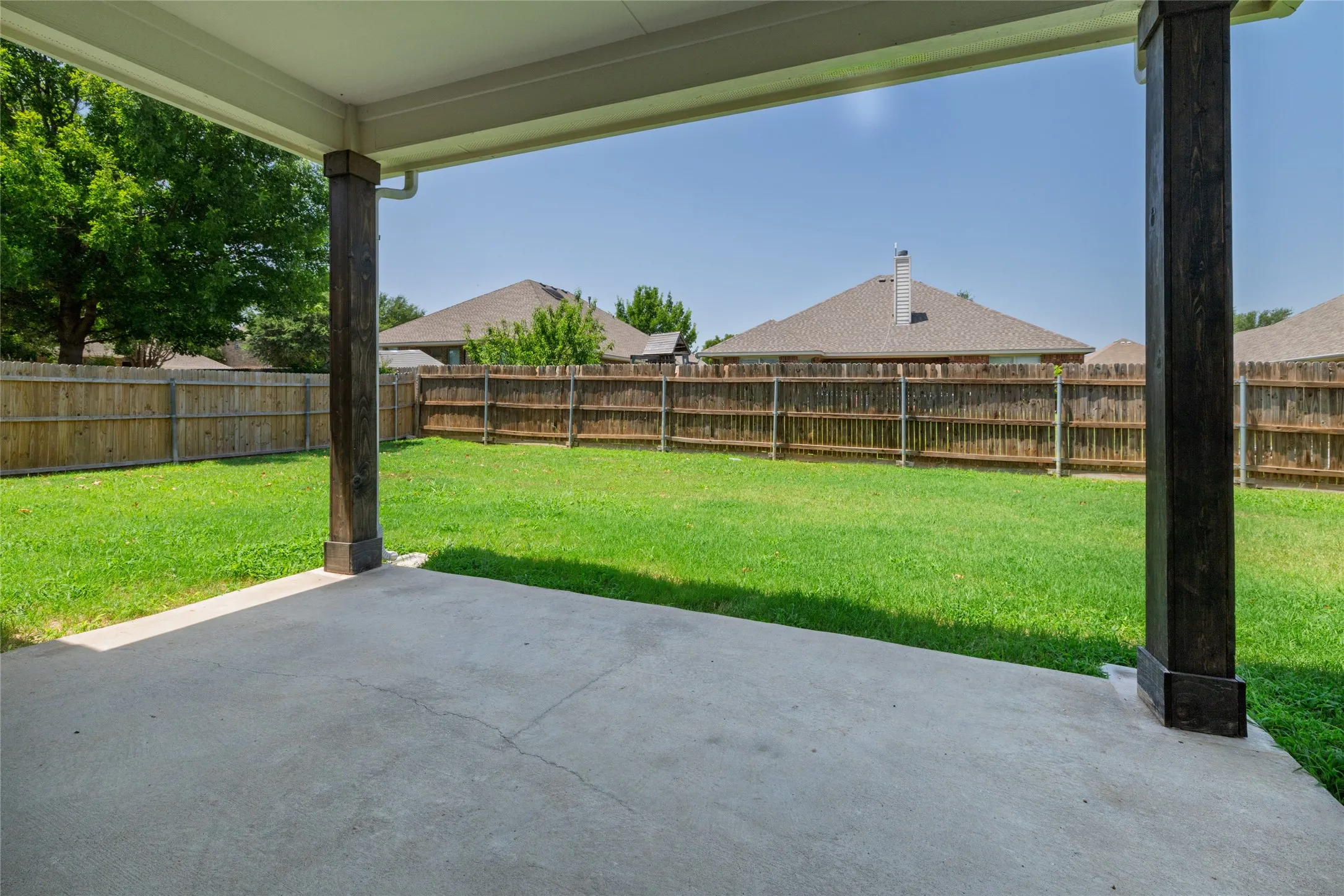Original Photo AI used - Covered concrete patio overlooking a spacious lawn, featuring a wood privacy fence and mature trees