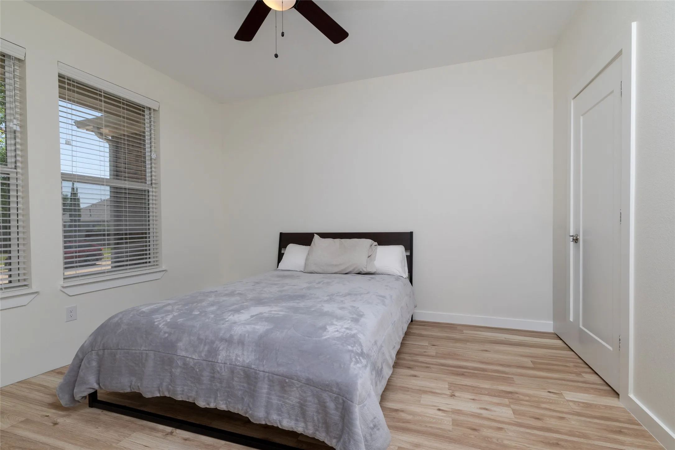 Front Bedroom - Perfect for office, Exercise room, or guest bedroom - featuring two windows with blinds, wood-finish flooring, a ceiling fan with integrated lighting, and a paneled door with a silver-tone handle