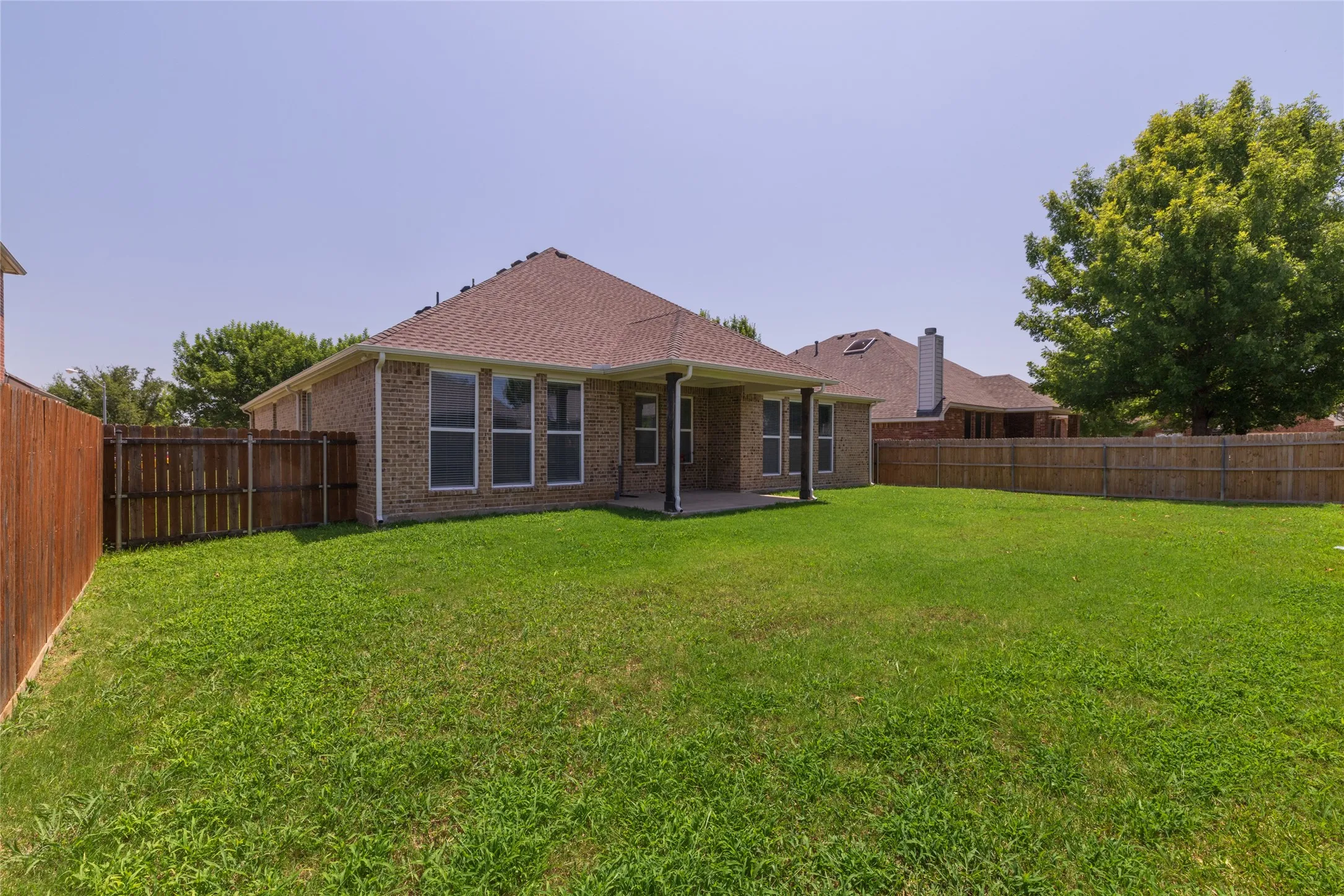 Expansive green lawn with a covered patio, brick exterior, and a privacy fence