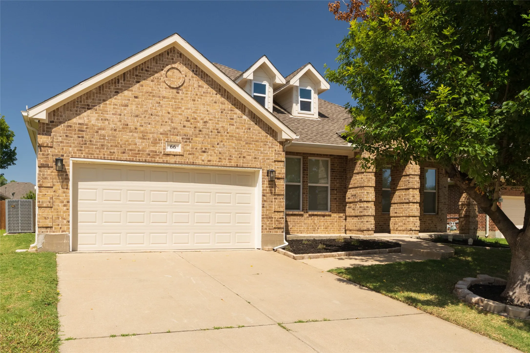 Brick exterior featuring a two-car garage, dormer windows, and a concrete driveway