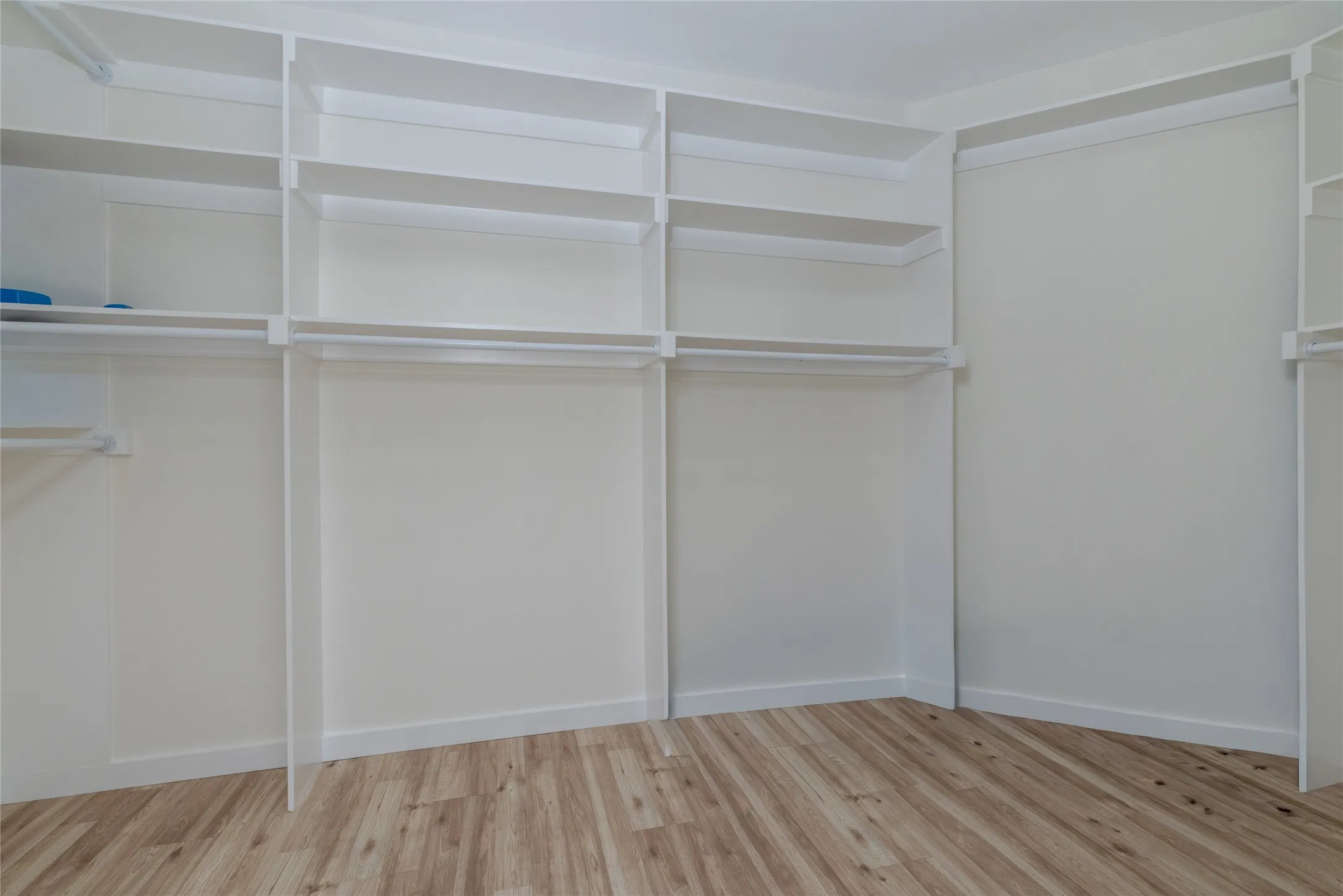 Custom closet system featuring white shelving and multiple hanging rods over wood-finish flooring