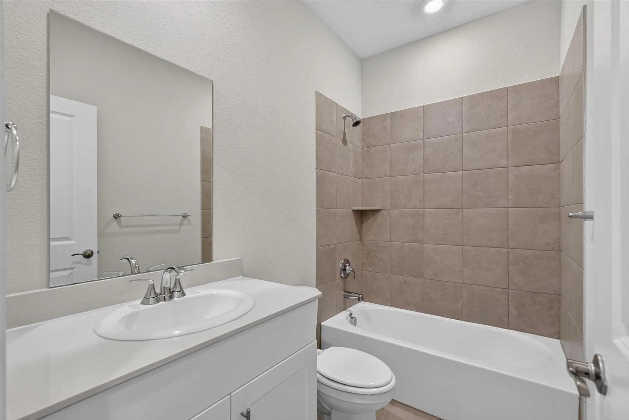 Bathroom featuring a white vanity with a rectangular undermount sink, a large wall-mounted mirror, brushed nickel fixtures, a white bathtub, and brown subway tile surround with a recessed niche