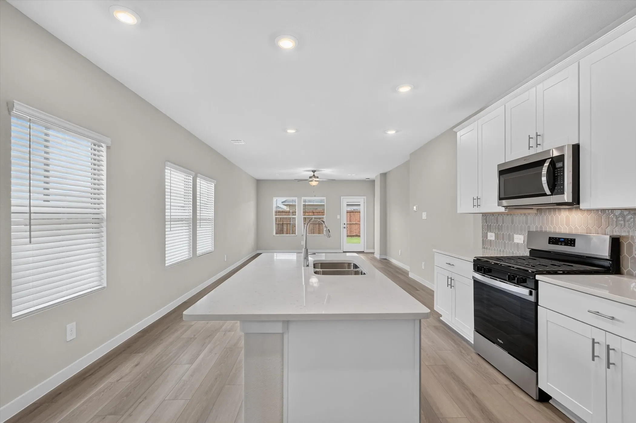Open-concept kitchen featuring an elongated island with an undermount sink, white cabinetry, stainless steel appliances, and a gray geometric tile backsplash