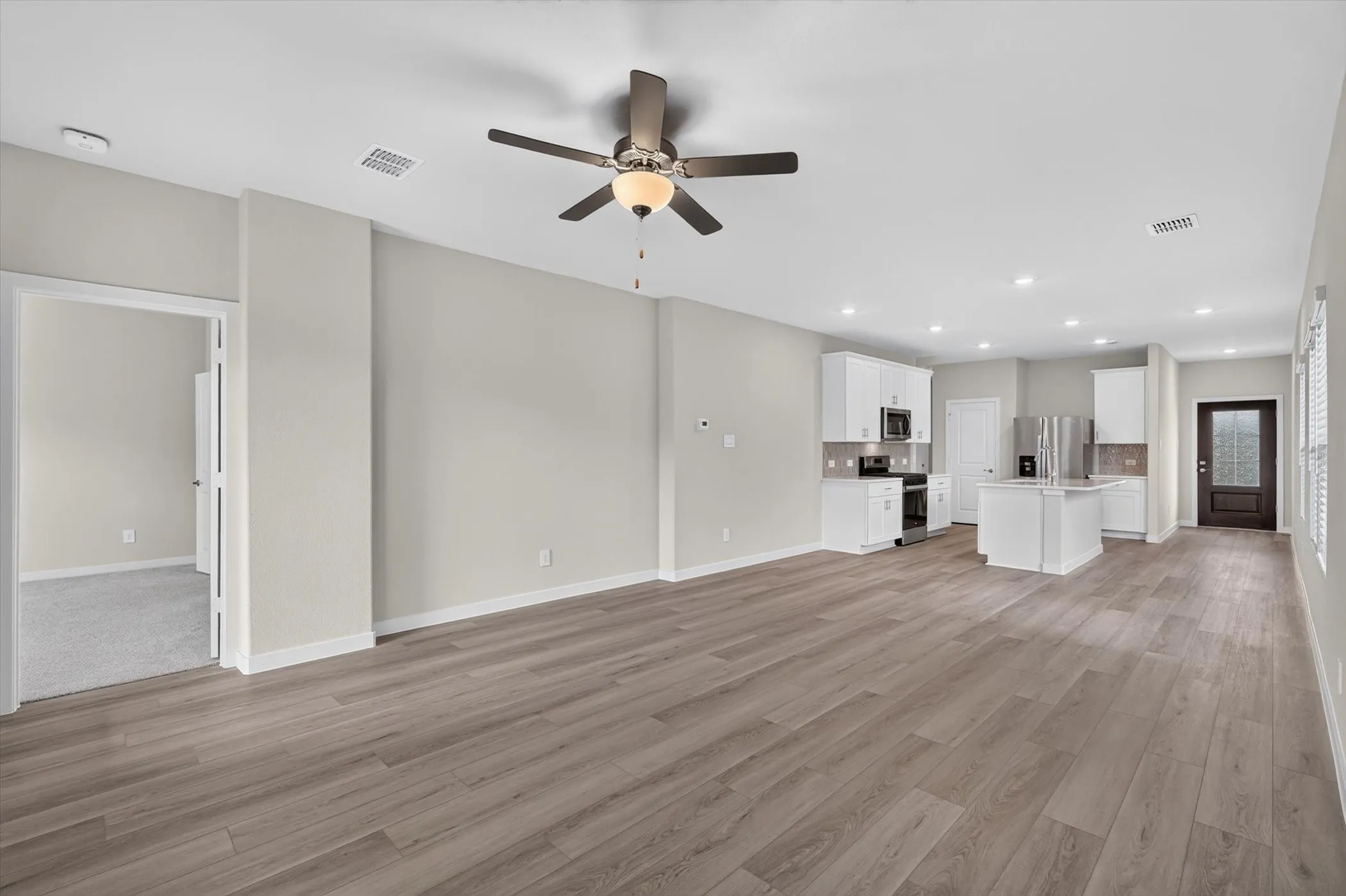 Spacious open-concept living area featuring wood-finish flooring, a ceiling fan with integrated lighting, and recessed lighting