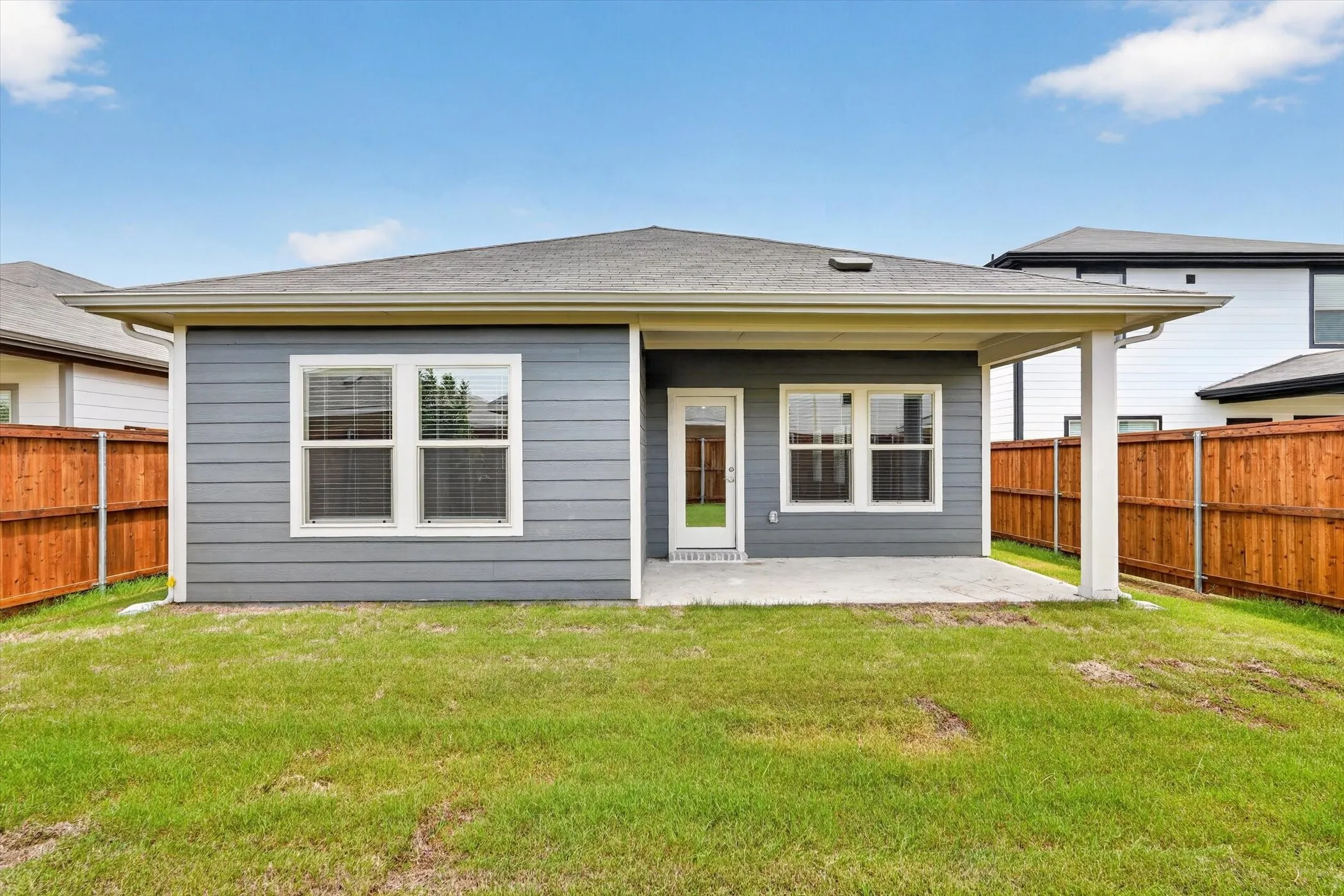 Expansive backyard featuring a manicured lawn, full privacy fencing, and a covered patio