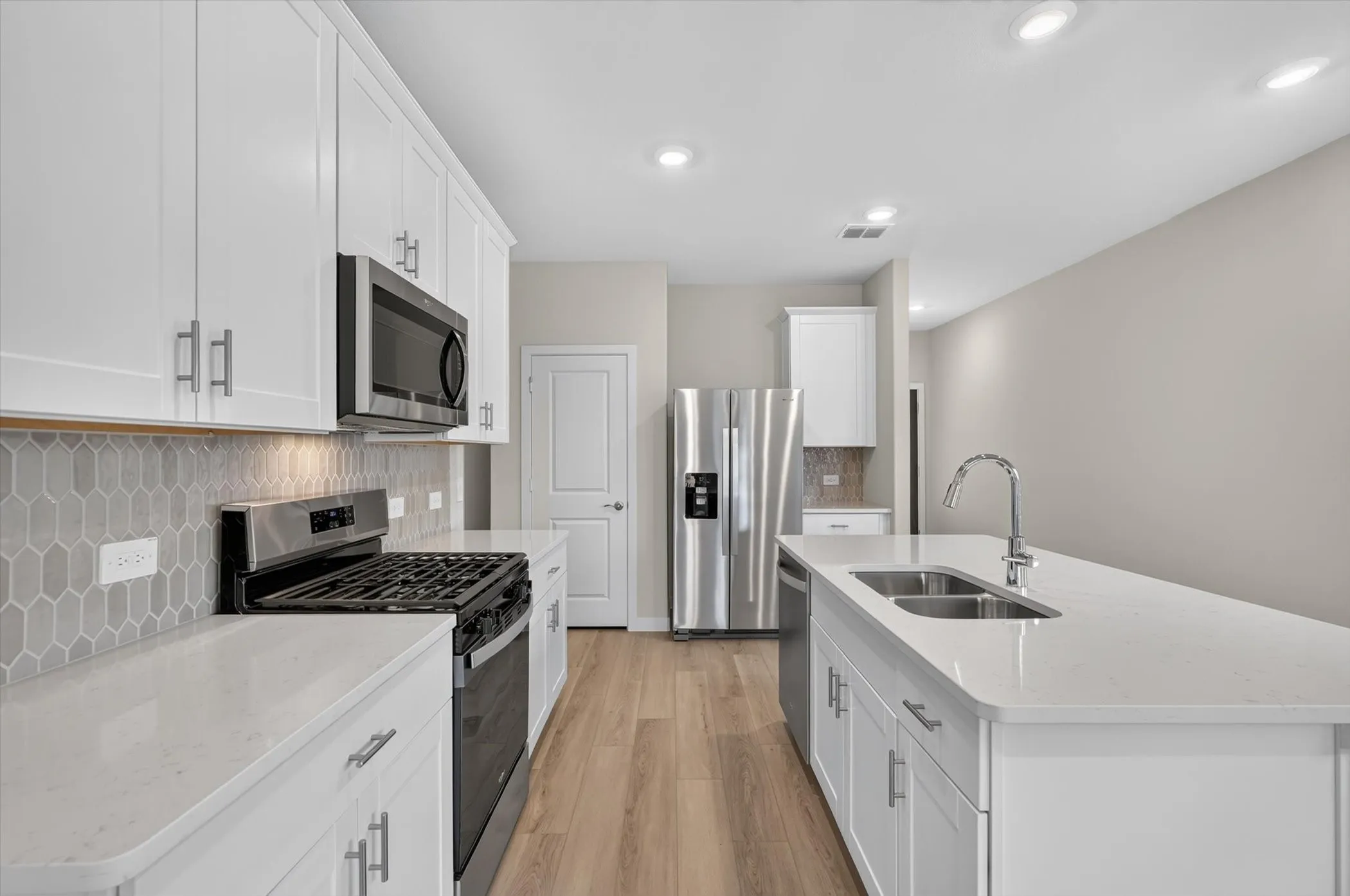 Modern kitchen featuring white cabinetry, light countertops, stainless steel appliances, a center island with double sink, and wood-finish flooring