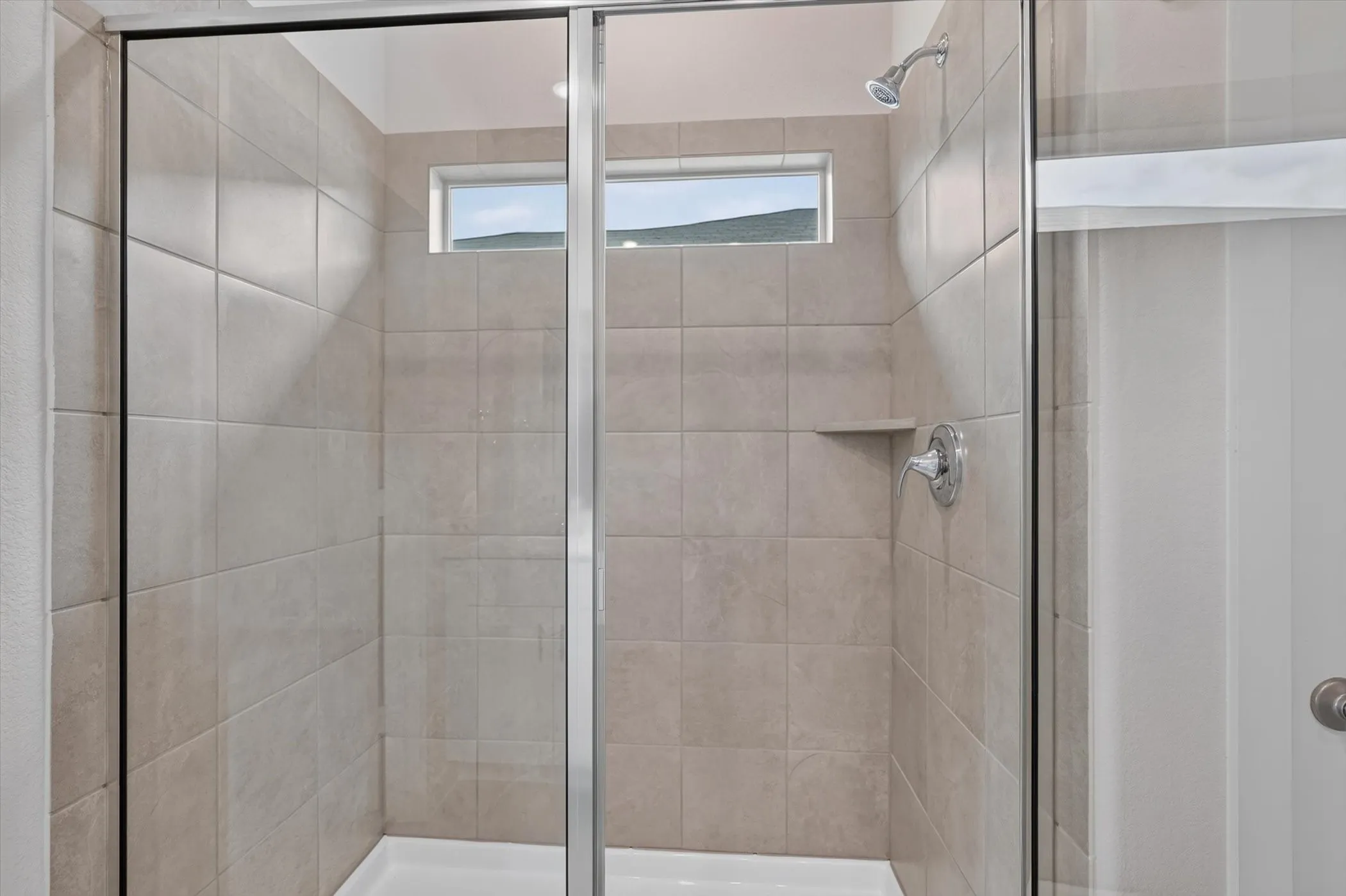 Shower enclosure featuring light-toned tile walls, a built-in shower niche, chrome fixtures, and frosted glass sliding doors