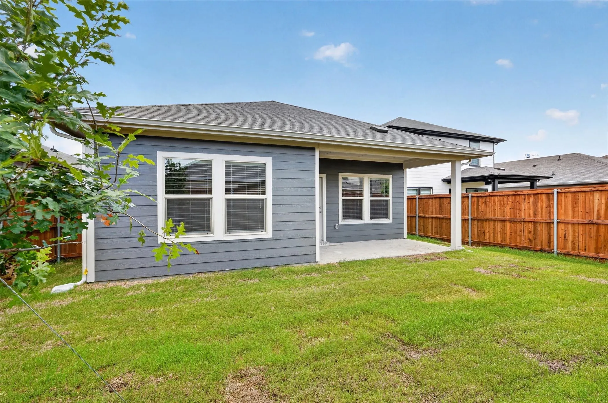 Expansive green lawn featuring a covered patio, gray siding, white trim windows, and a wood privacy fence