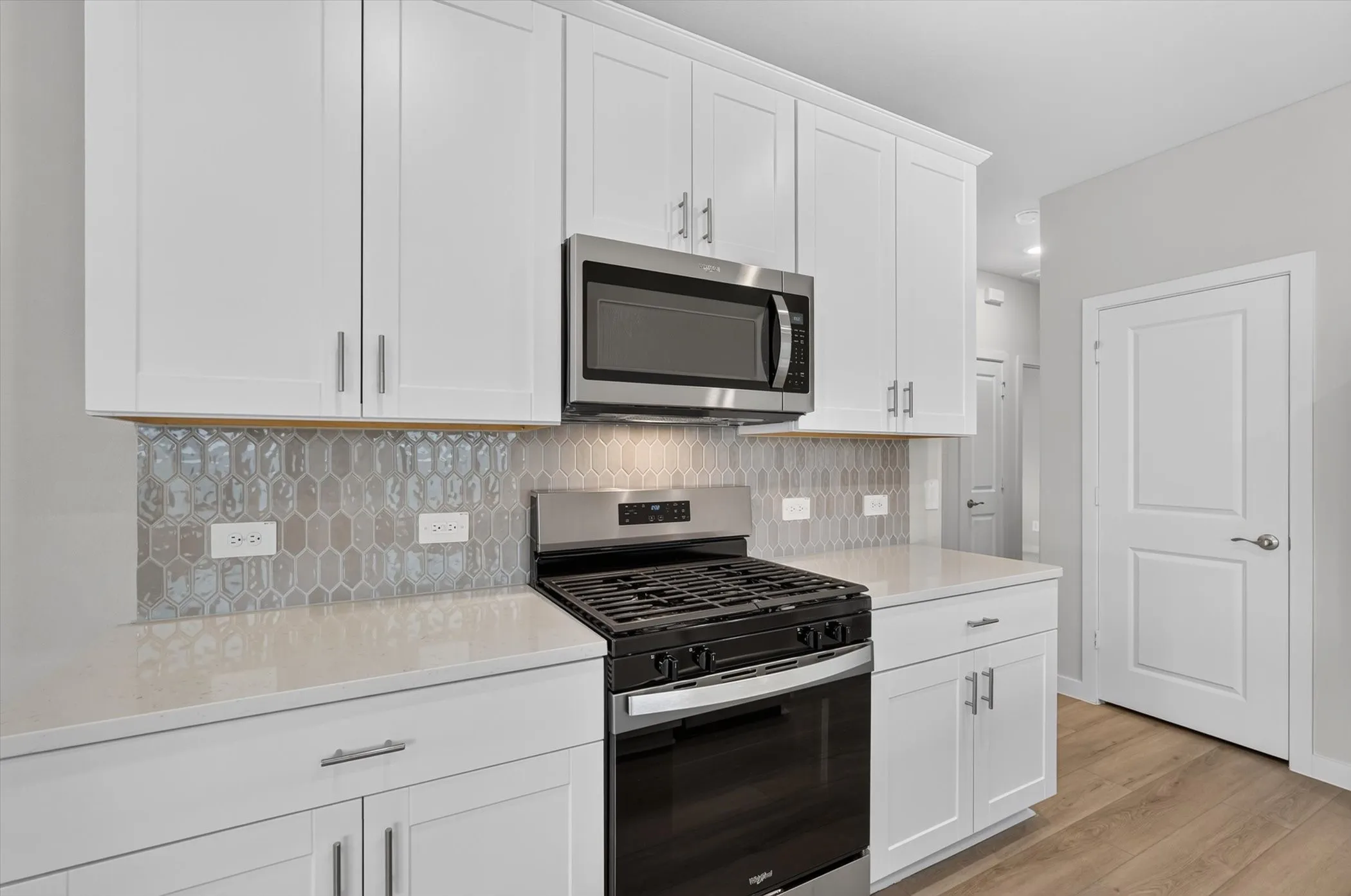 Kitchen featuring white shaker cabinetry, stainless steel microwave, gas range, light countertops, and a decorative tile backsplash
