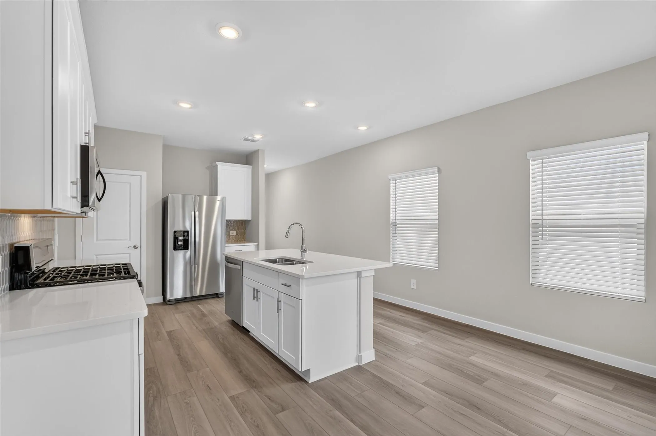 Contemporary kitchen featuring a central island with an undermount sink, white cabinetry, stainless steel appliances, and wood-finish flooring