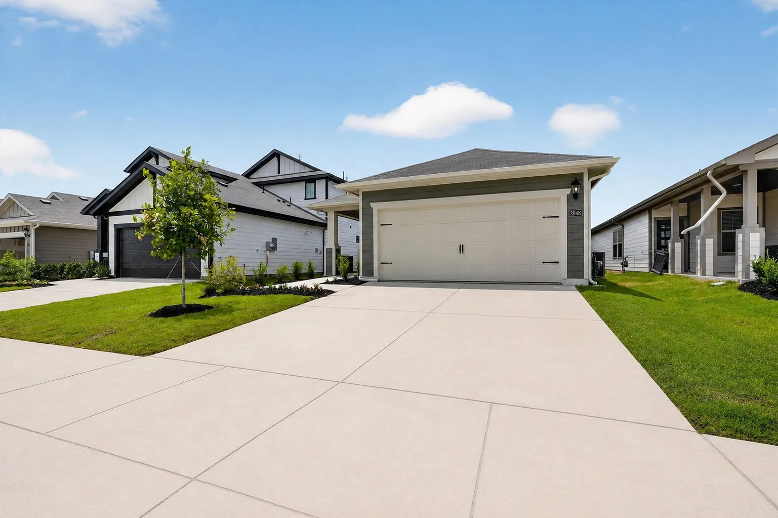 Newly constructed residence featuring a spacious concrete driveway, attached two-car garage with neutral-finish door, modern architectural design with mixed exterior finishes, and professionally landscaped front grounds with mature plantings and manicured lawn