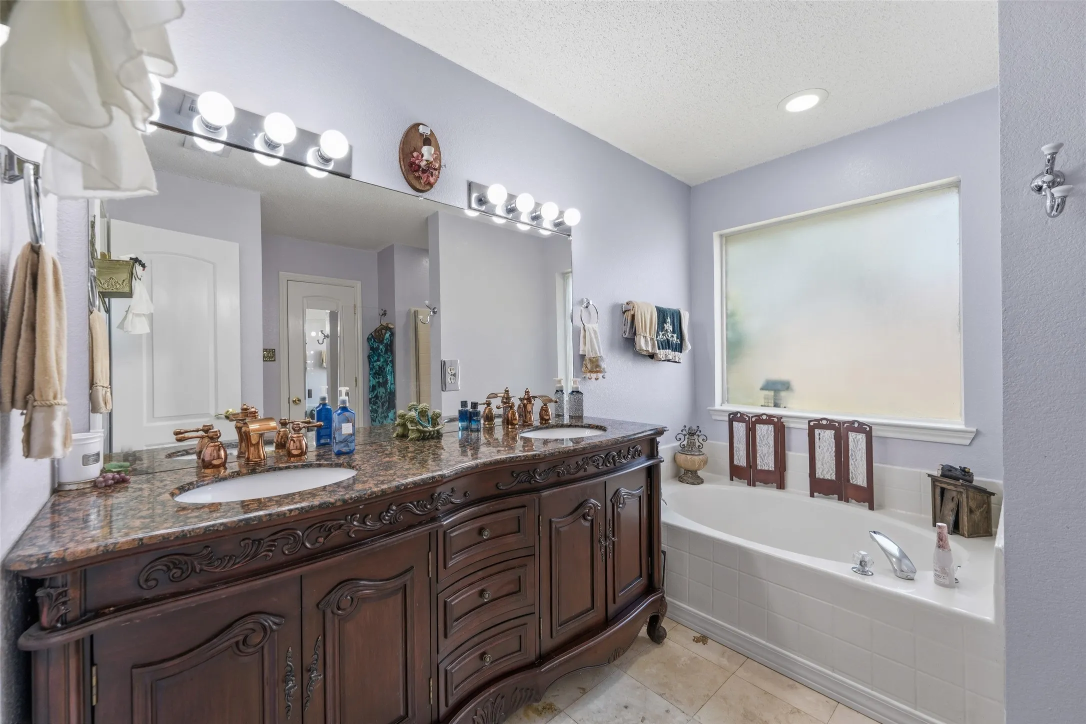 Dual vanity with a stone countertop and integrated sinks, under-mounted jetted bathtub, recessed ceiling lighting, and frosted window