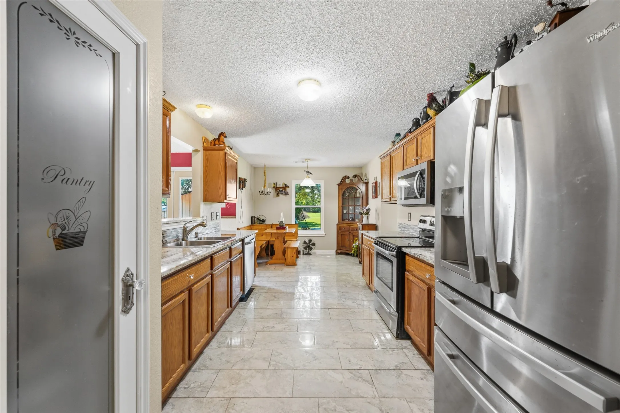 Kitchen featuring stainless steel appliances, wood cabinetry, stone countertops, and tile flooring