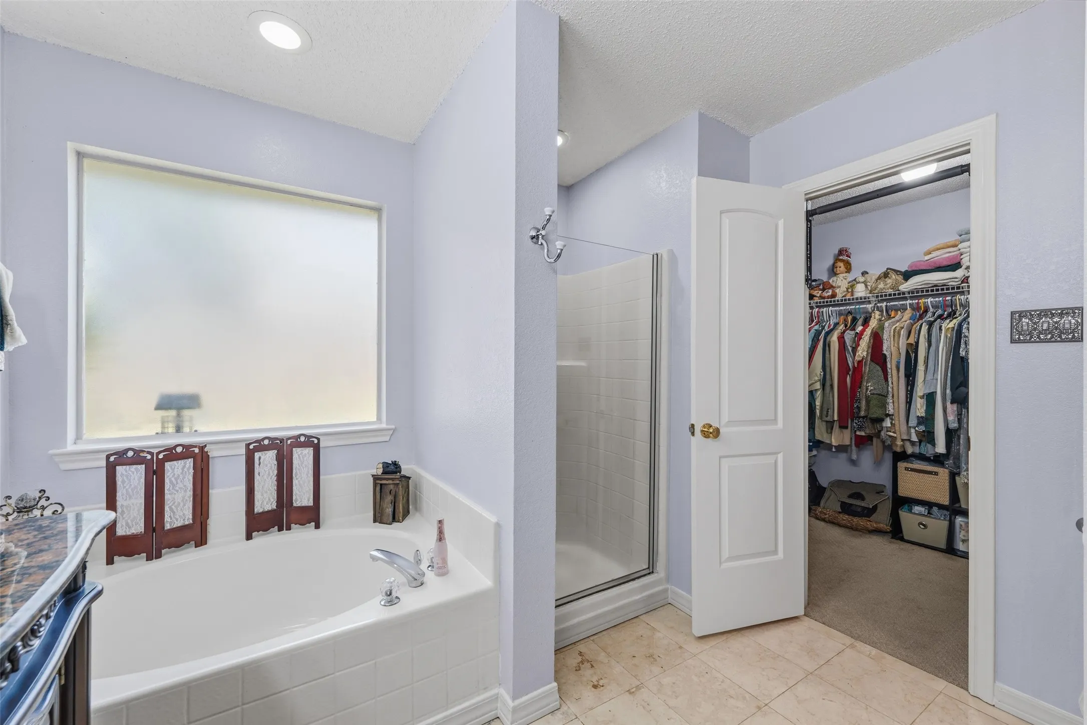 Soaking tub with a large frosted window, glass-enclosed shower, and a walk-in closet