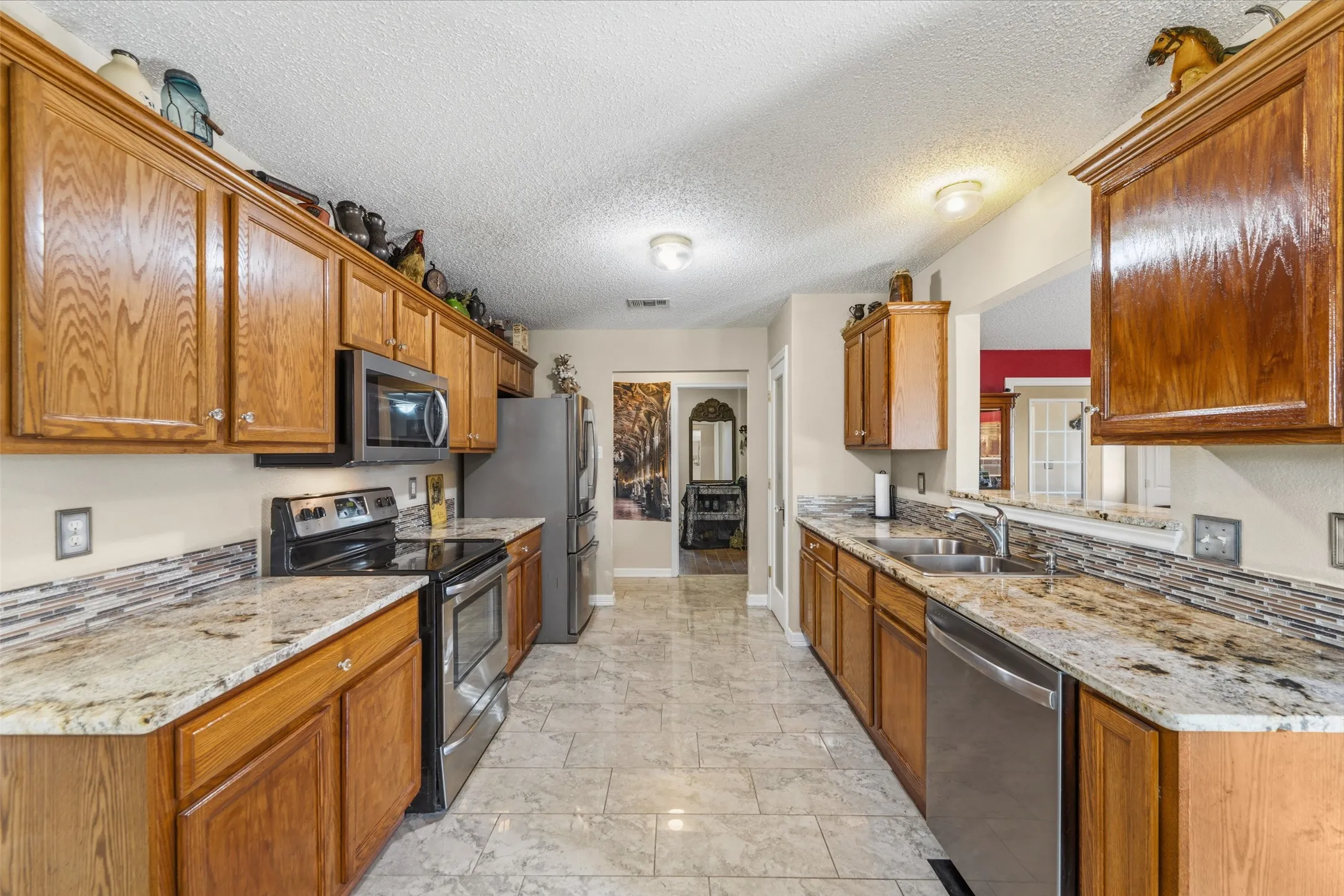 Galley kitchen featuring wood cabinetry, stainless steel appliances, granite countertops, and a mosaic tile backsplash