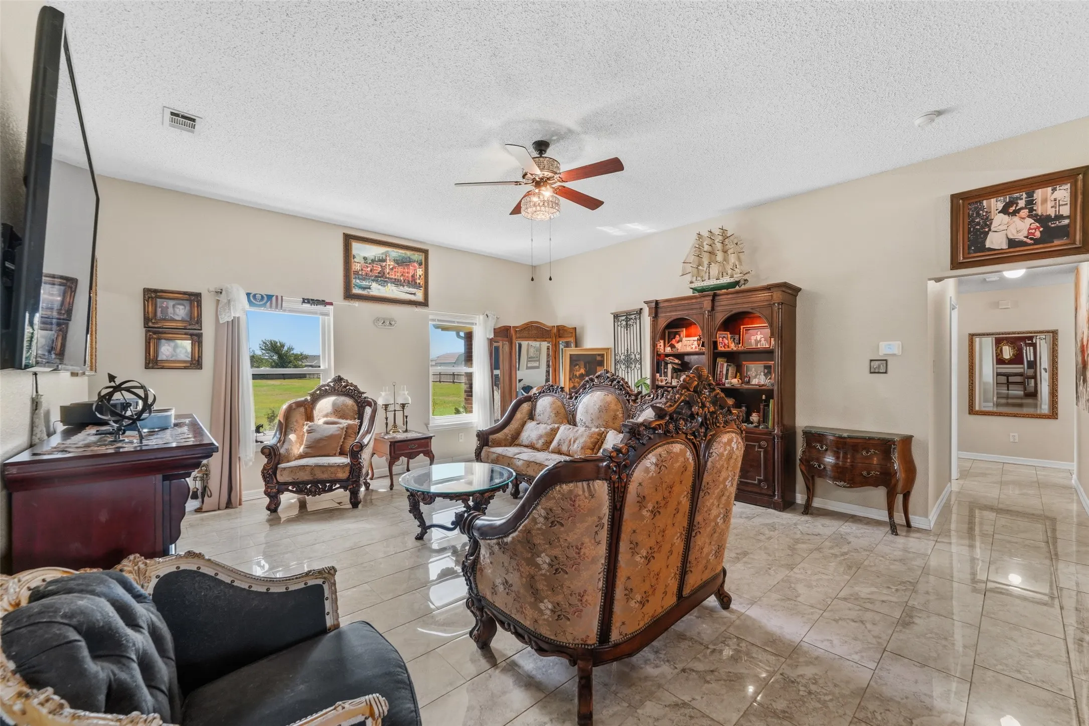 Spacious living area featuring light-toned walls, a decorative ceiling fan, and large windows providing abundant natural light