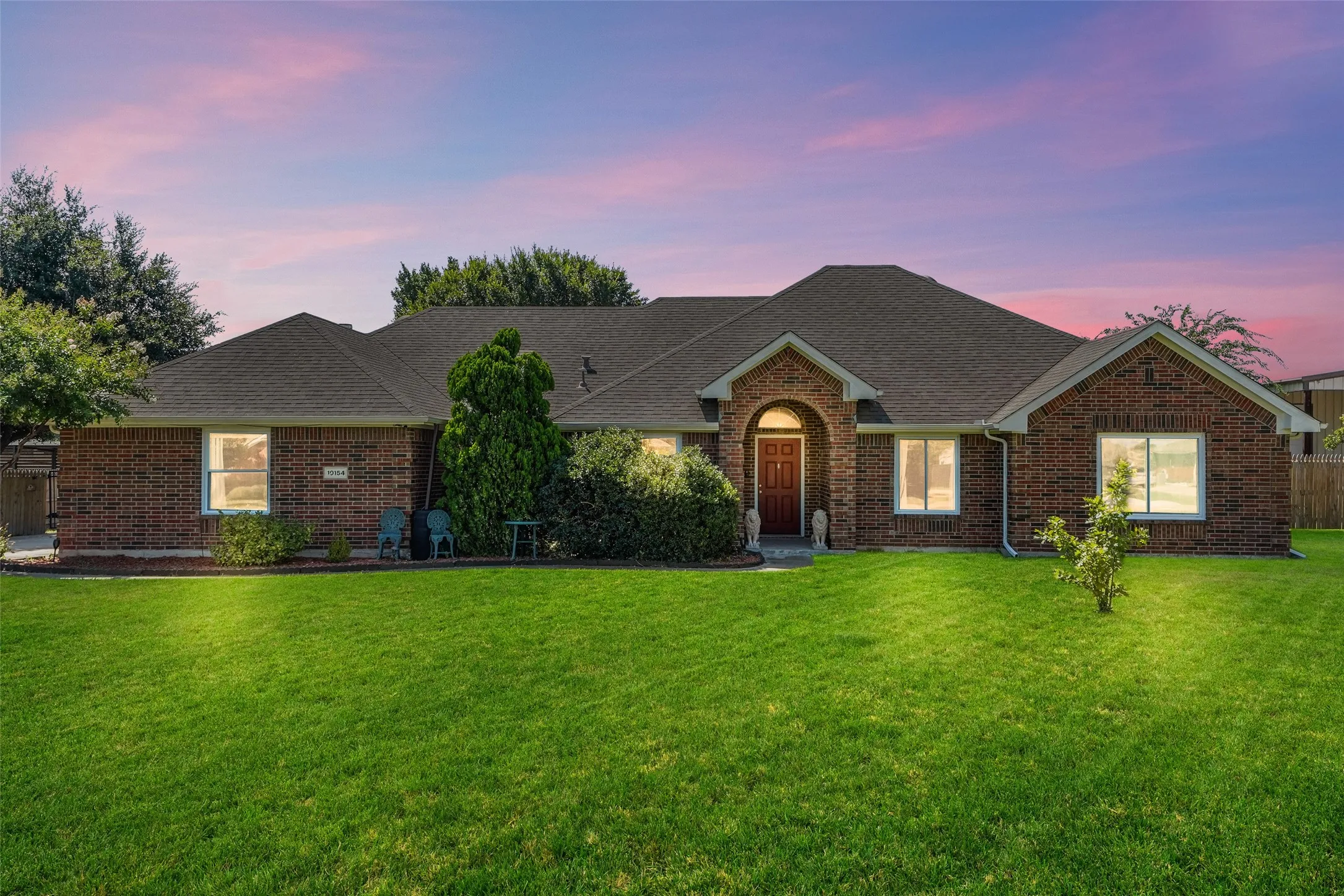 Brick exterior home featuring an arched entryway with a red-toned door, a dark shingle roof, and multiple large windows