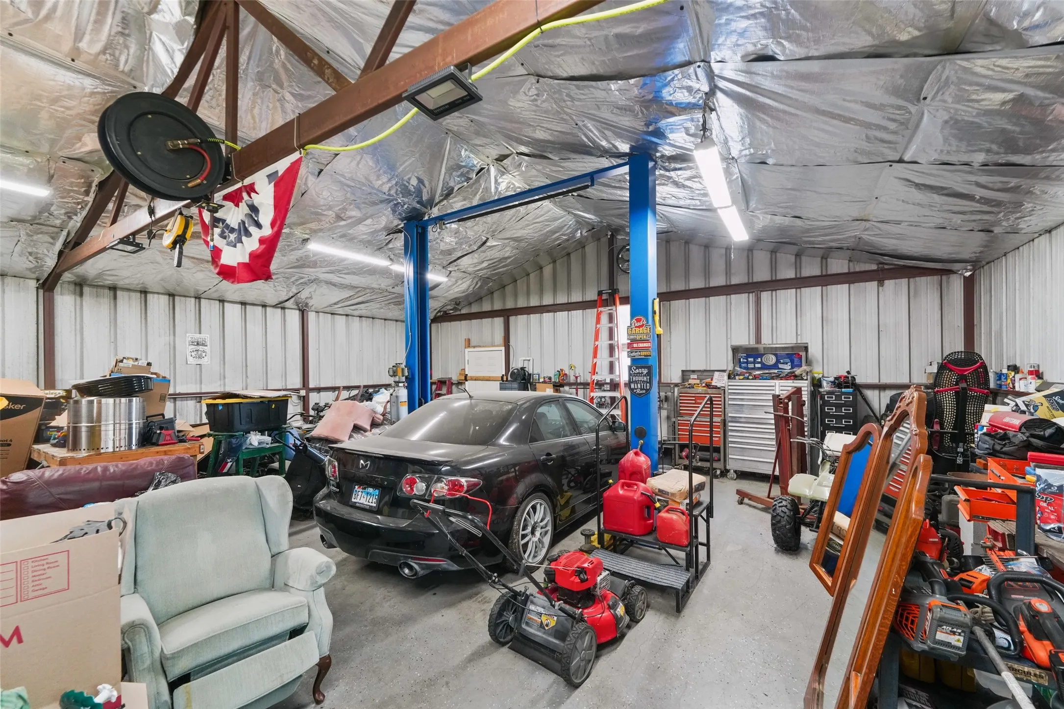 Spacious workshop featuring a metal frame, corrugated metal walls, concrete flooring, and a vehicle lift