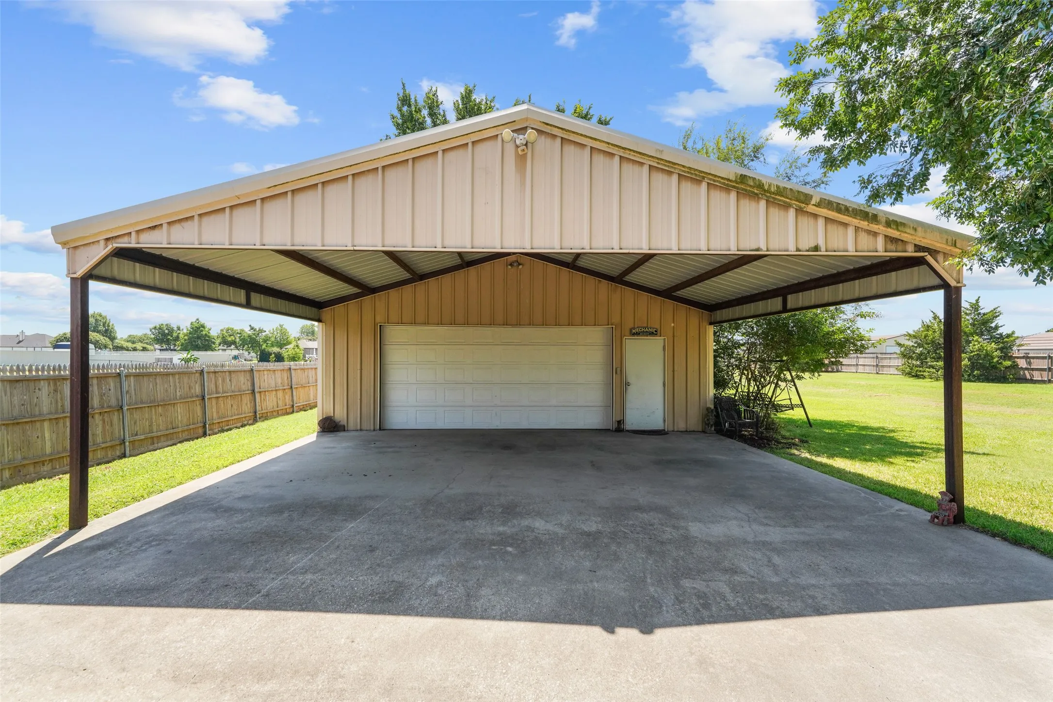 Detached metal garage structure featuring an integrated carport, a roll-up garage door, a pedestrian entry door, and a spacious concrete pad