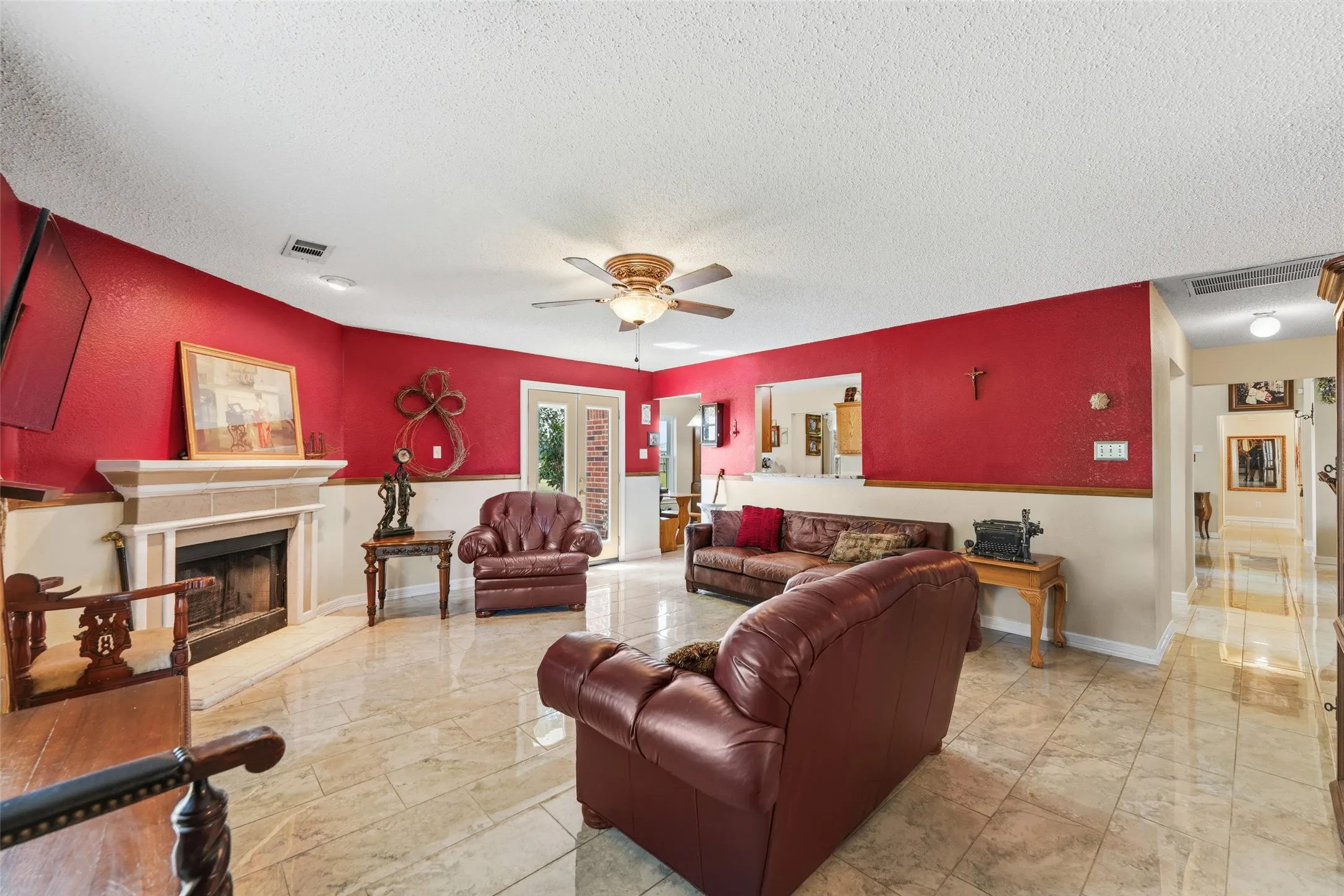 Spacious living area featuring polished tile flooring, a built-in fireplace with a stone mantel, a ceiling fan with integrated lighting, and French doors providing exterior access