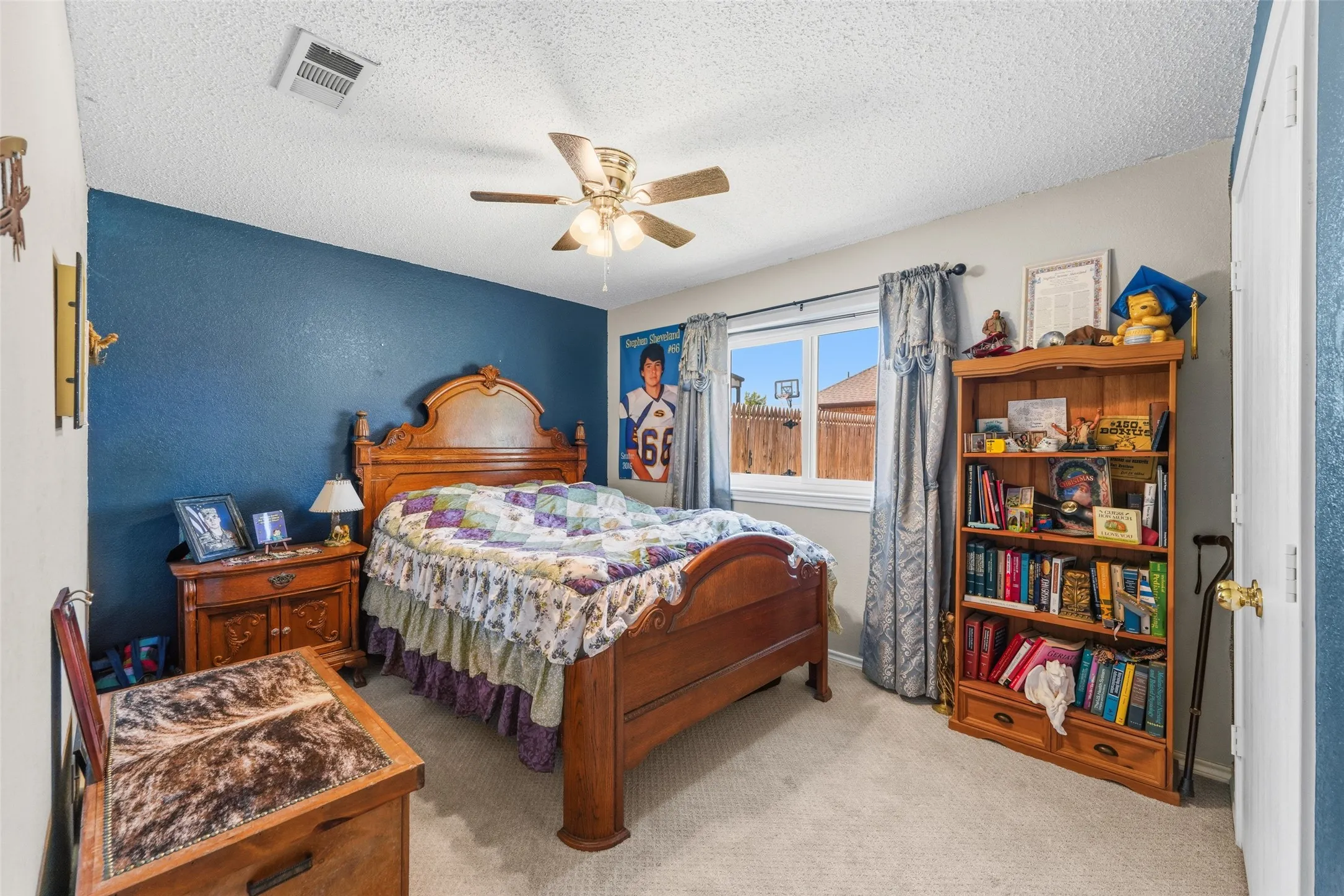 Carpeted room featuring a ceiling fan, a window with exterior fencing, a built-in closet, and a wooden bookcase