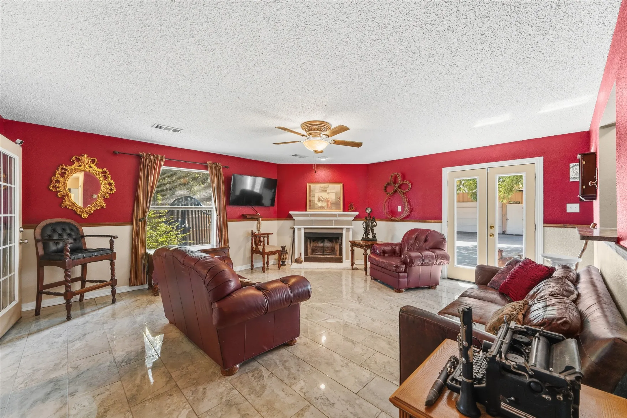 Spacious living area featuring light-toned tile flooring, a corner fireplace with a white mantle, and a ceiling fan with integrated lighting