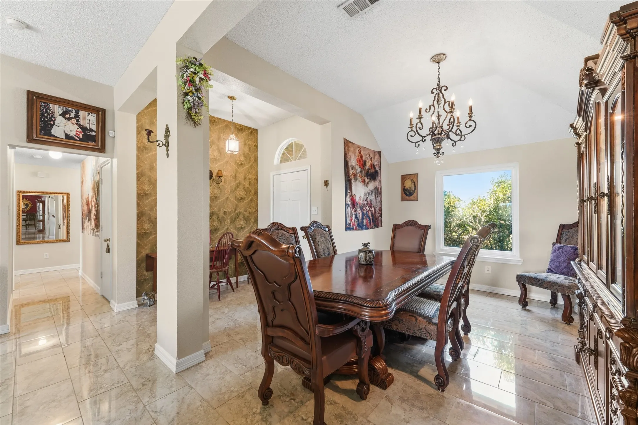Vaulted ceiling with an ornate chandelier, tile flooring, and a large window