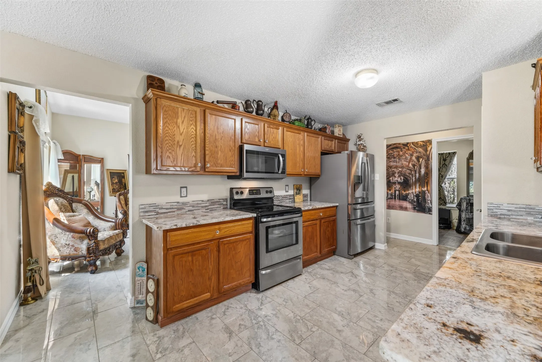 Kitchen featuring wood cabinetry, stainless steel appliances, granite-style countertops, mosaic tile backsplash, and tile flooring