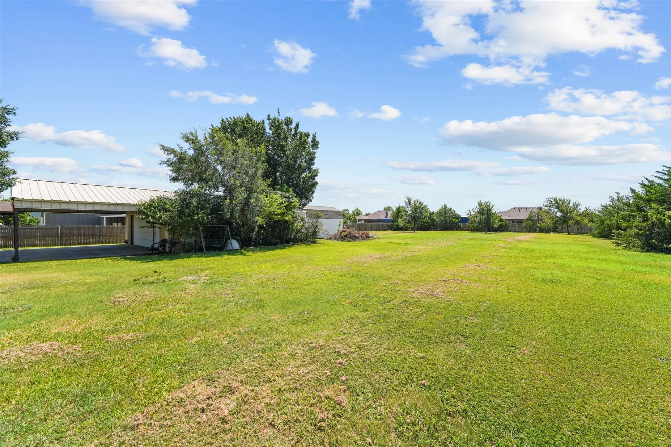 Expansive green lawn with a covered parking structure, privacy fencing, and mature perimeter trees