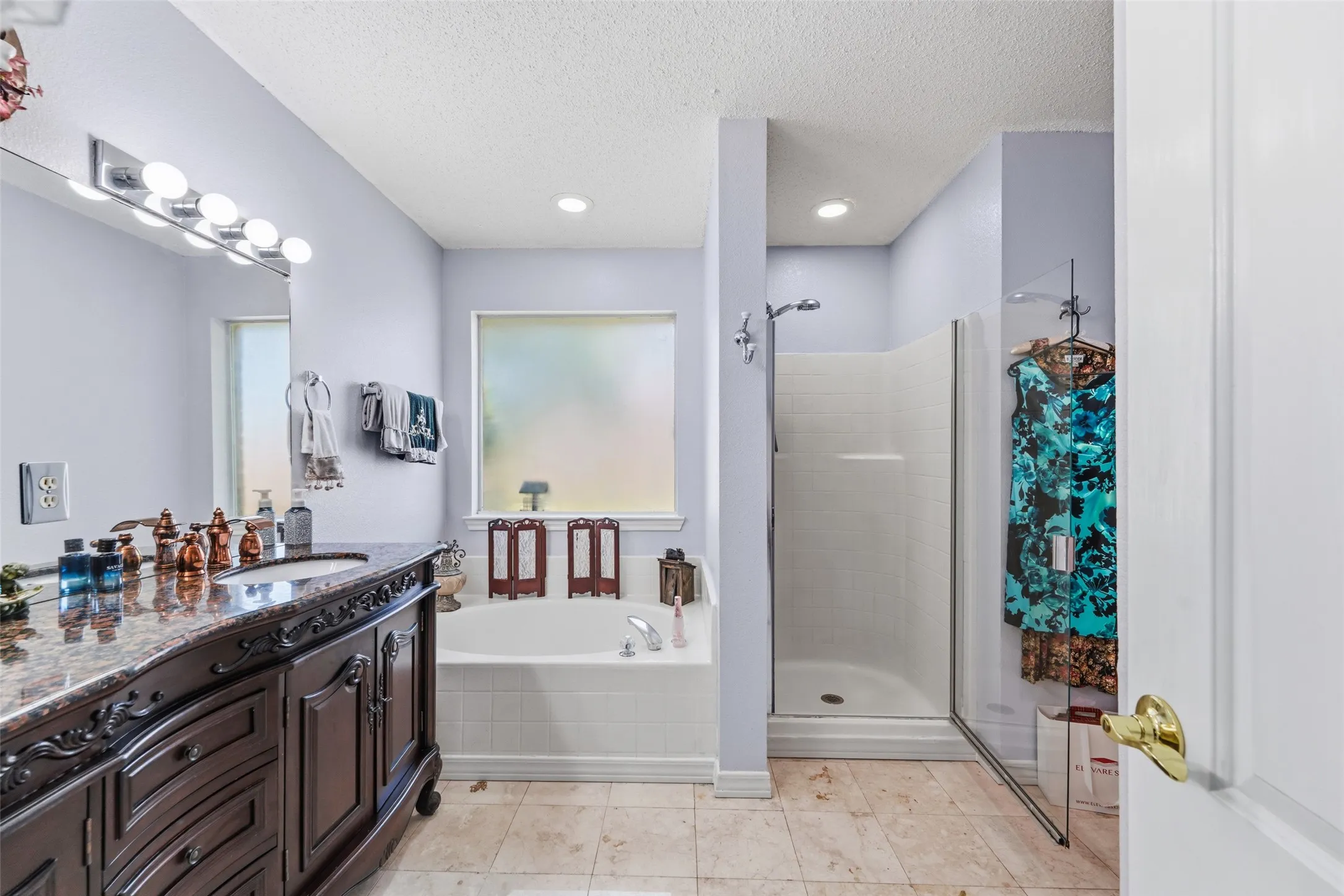 Full bathroom featuring a dark wood-finish vanity with a stone countertop and integrated sink, a built-in tub with tile surround, a separate shower with a clear glass enclosure, and light-colored tile flooring