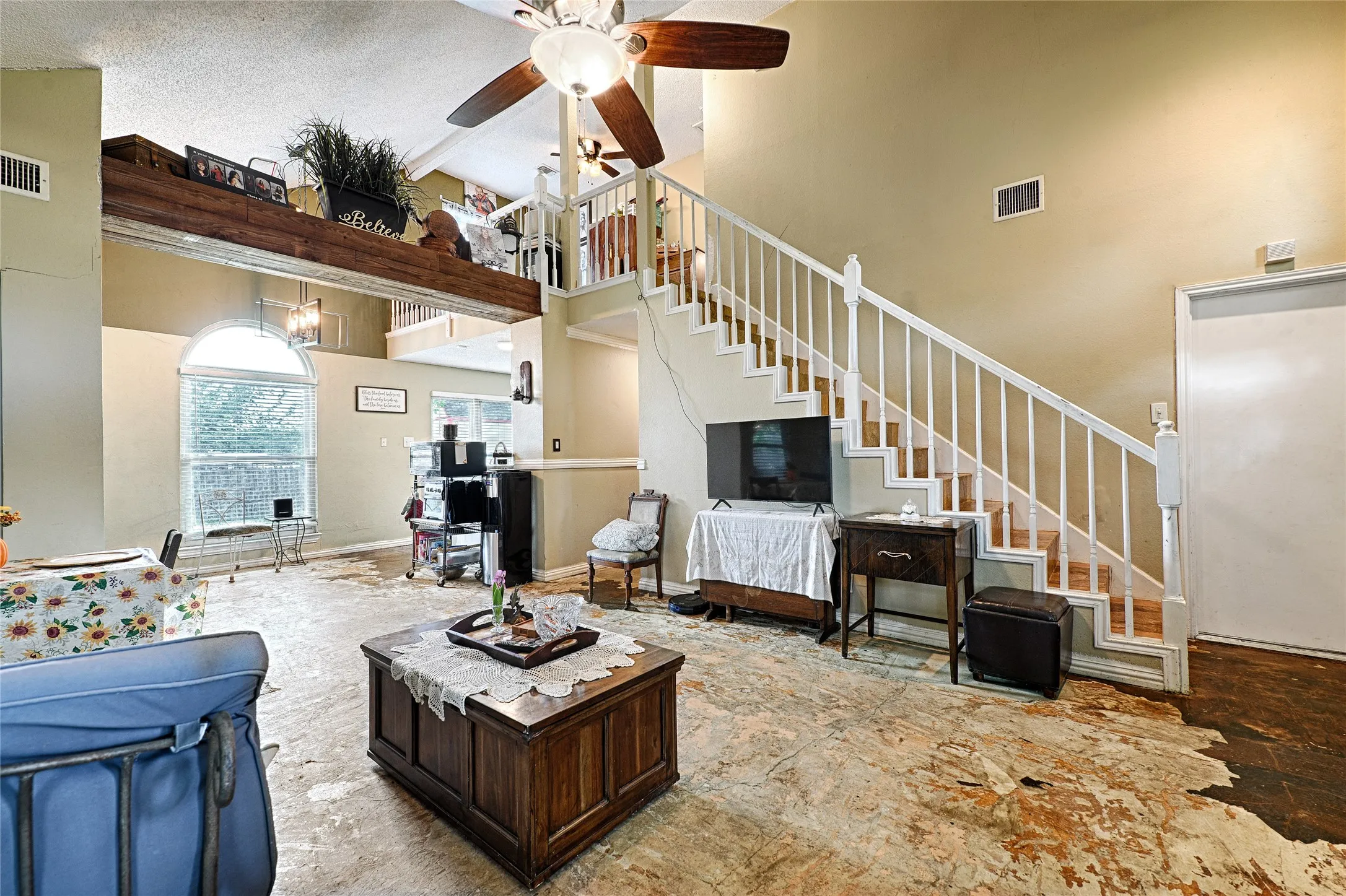 Vaulted ceilings with a ceiling fan, white spindle staircase, and a large arched window