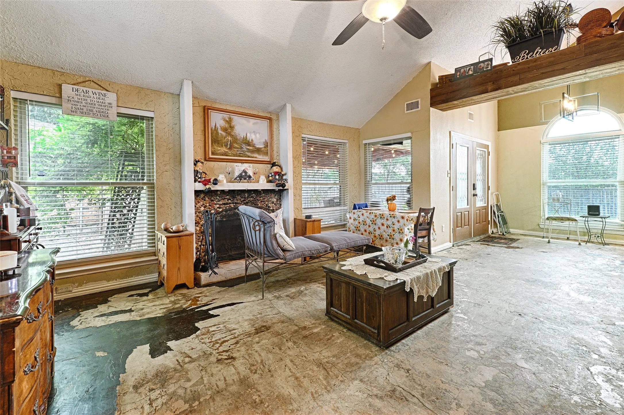 Spacious living area featuring a vaulted ceiling with a ceiling fan, a stone fireplace, and ample natural light from multiple windows