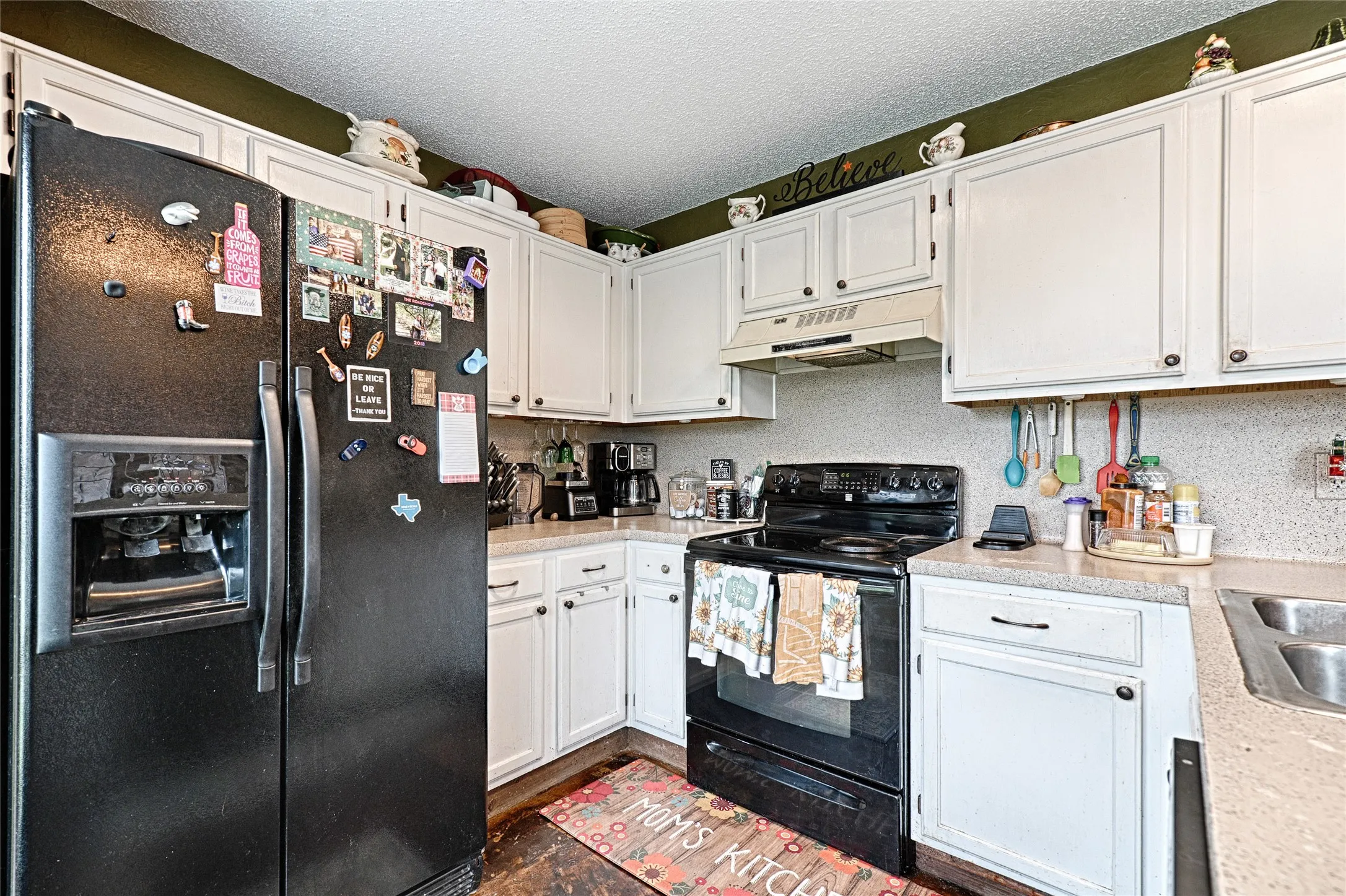 Kitchen featuring white cabinetry with dark hardware, black appliances, light-toned countertops, and a double-basin sink