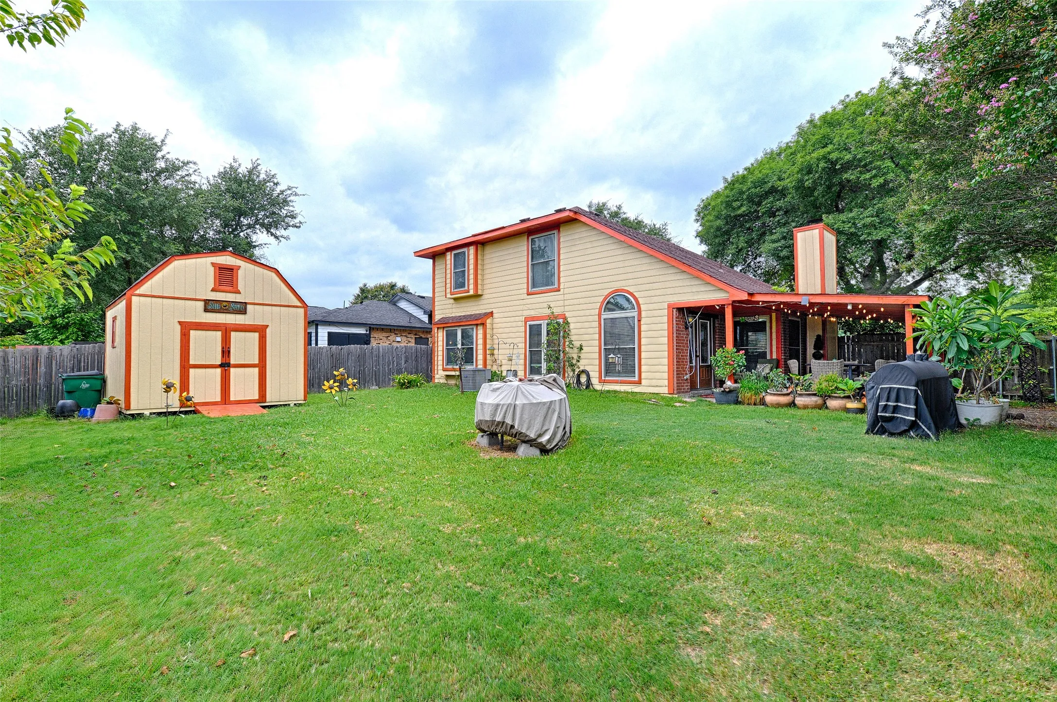 Spacious backyard featuring a large lawn area, a detached storage shed with double doors, and a covered patio with string lighting
