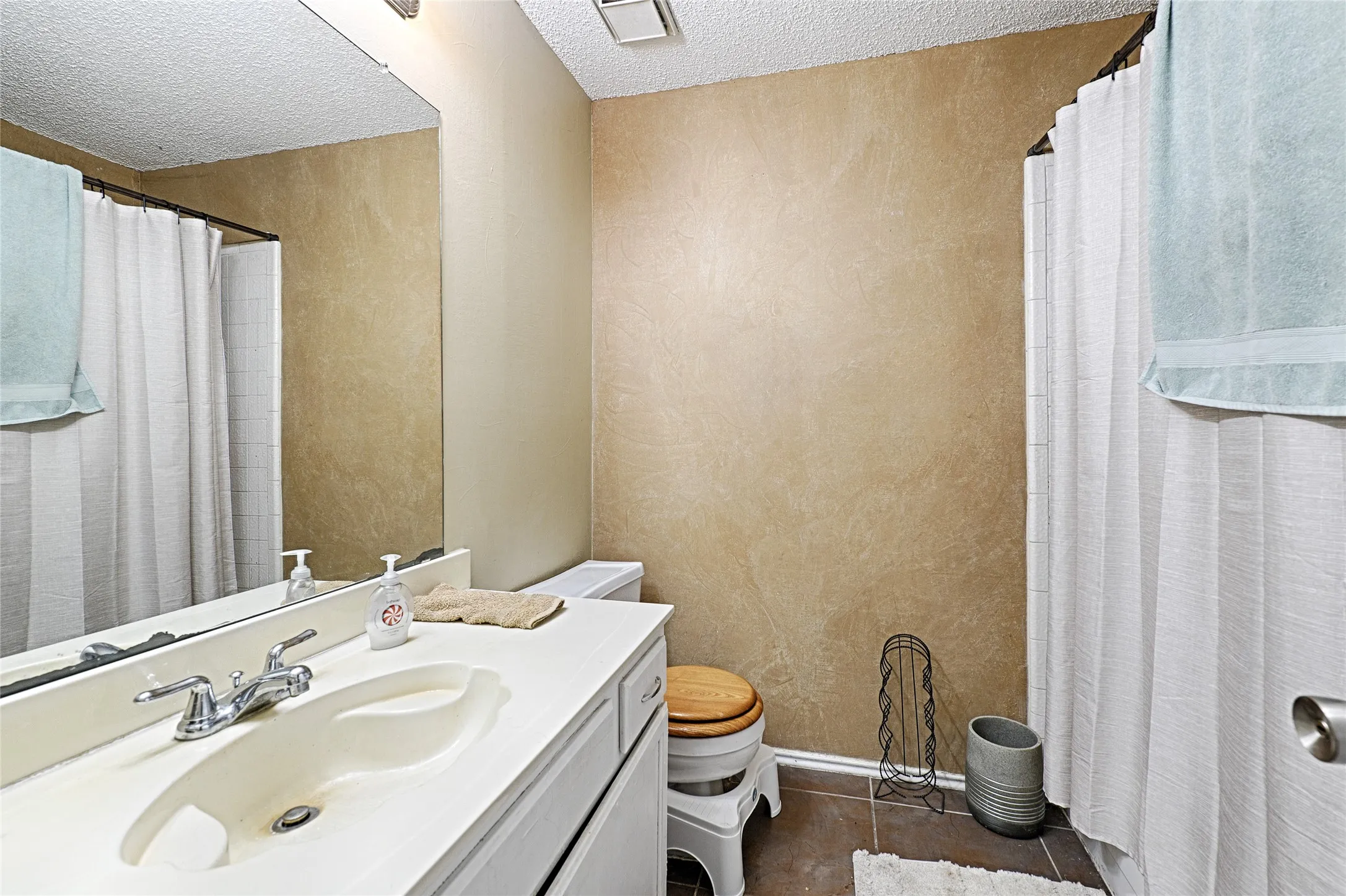 Bathroom featuring a single vanity with an integrated sink, chrome faucet, wall-mounted mirror, and a shower area with a white curtain